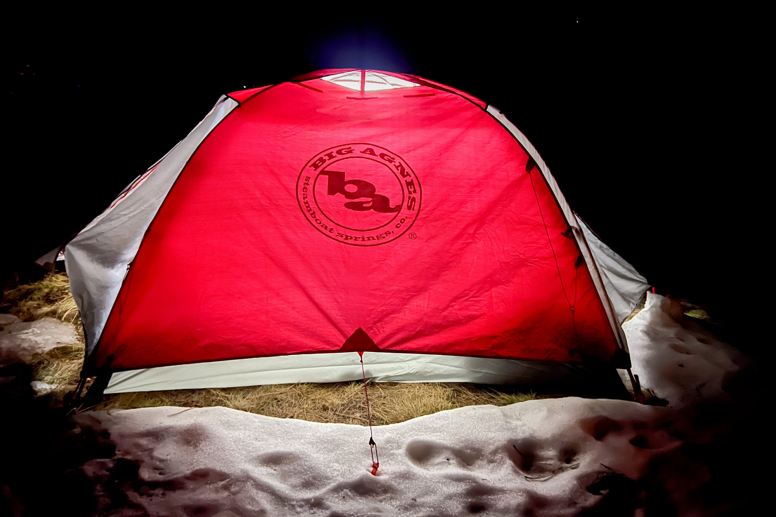 Big Agnes Copper Spur Expedition tent glowing red at night in a snowy setting with a reflective logo visible.