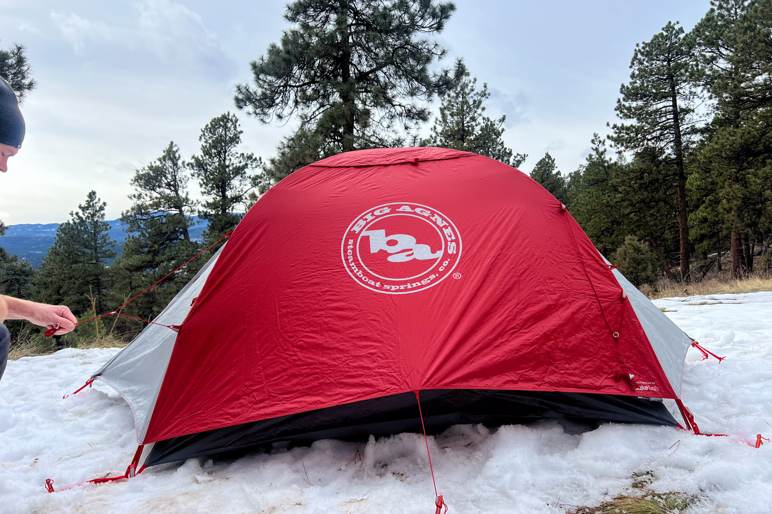 Big Agnes Copper Spur Expedition tent with a red rainfly set up in a snowy forest during daylight.