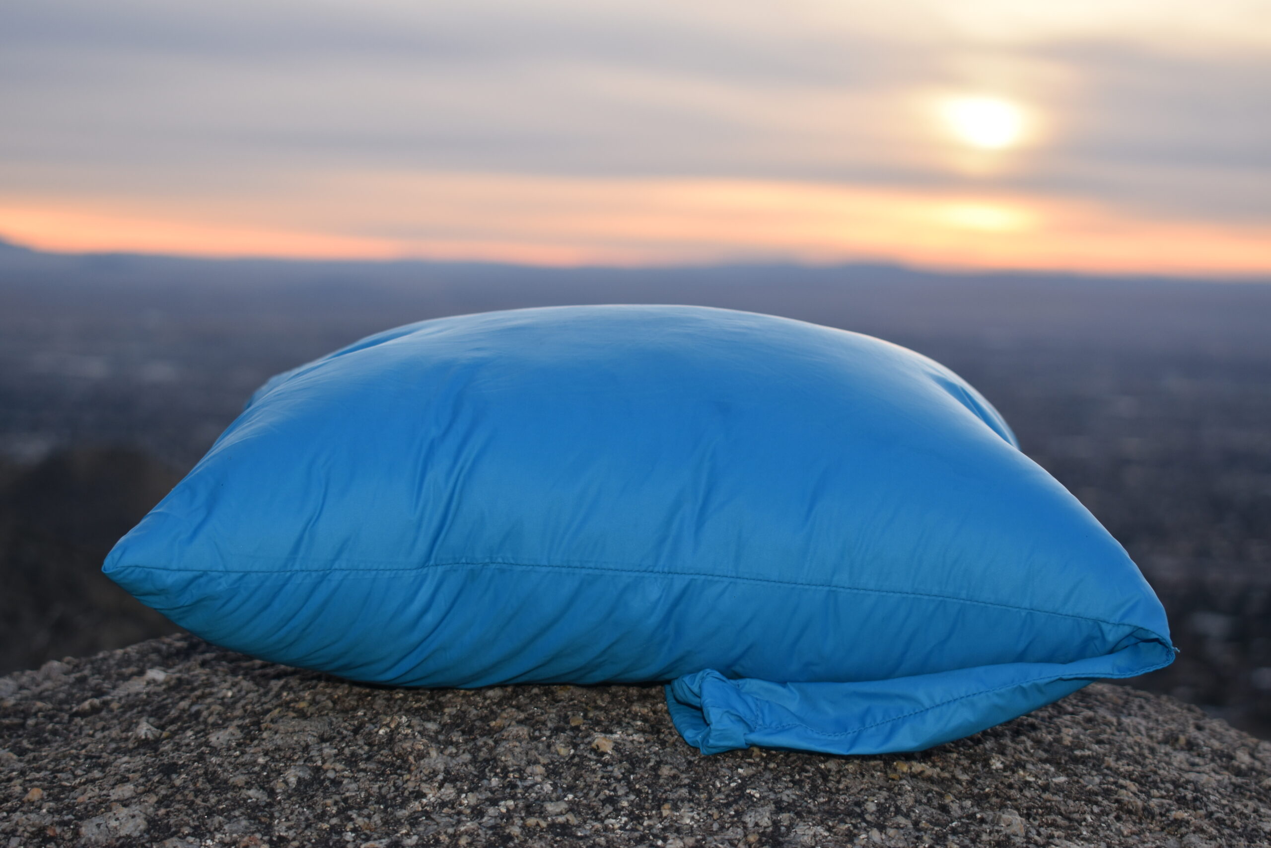 Close up of the Cloudrest Down Pillow on a rock with the sun setting on the horizon