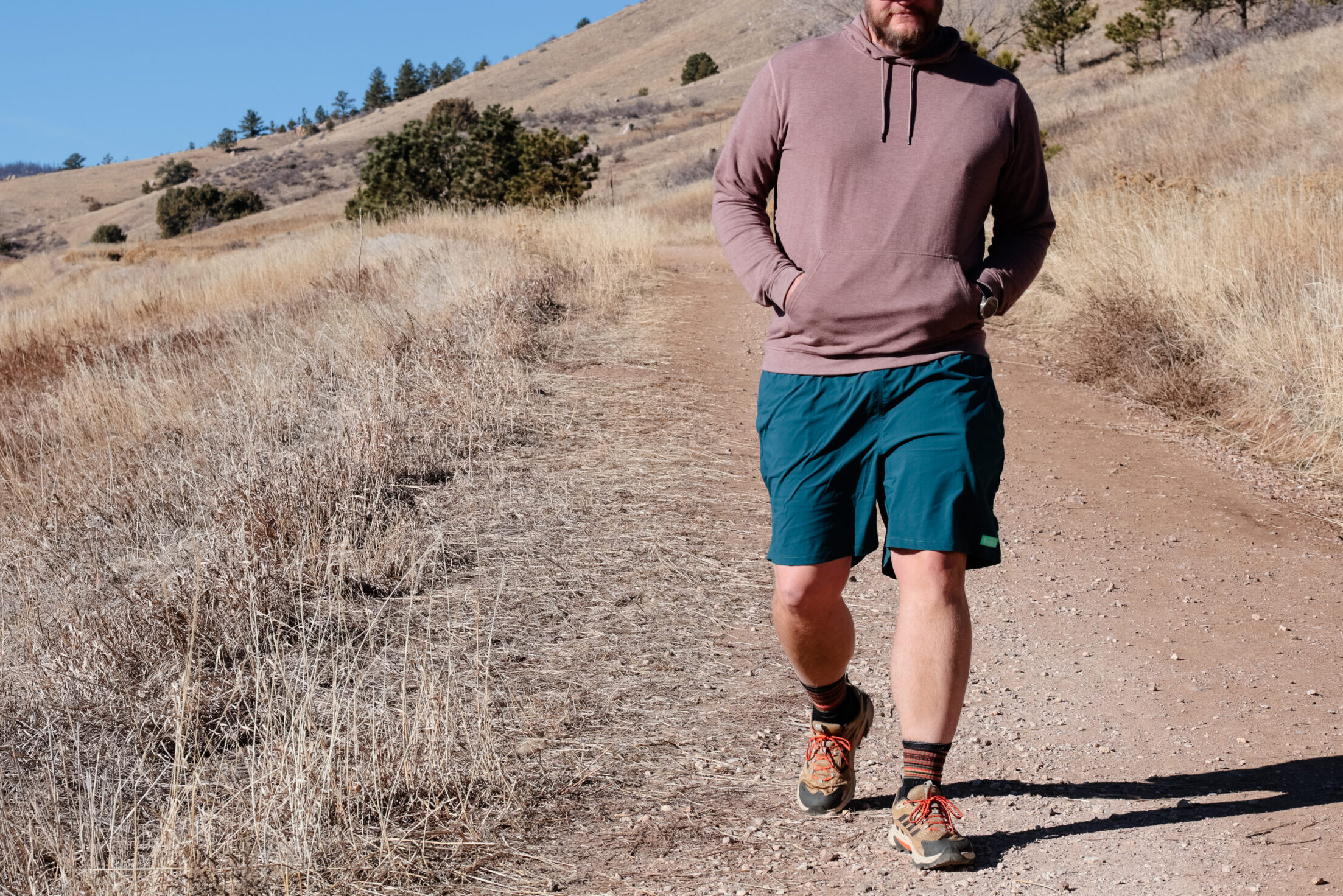 A man hiking down a trail in shorts and a hat.