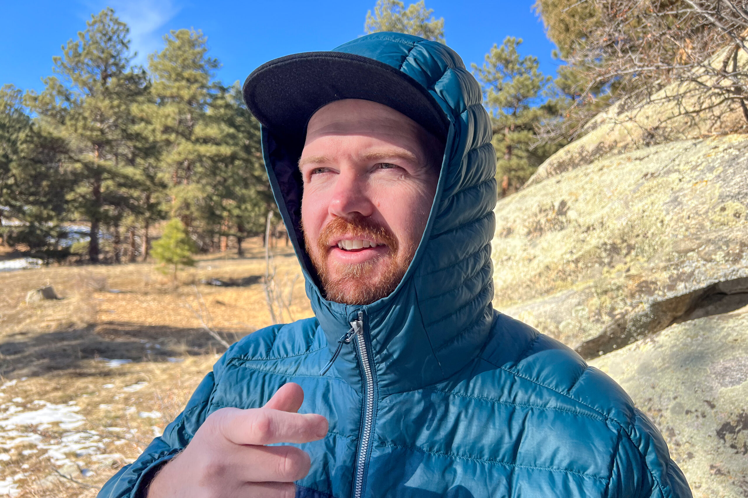 Close-up of a man wearing the hood of the Cotopaxi Fuego Down Jacket, standing in a forest with sunlight filtering through the trees.