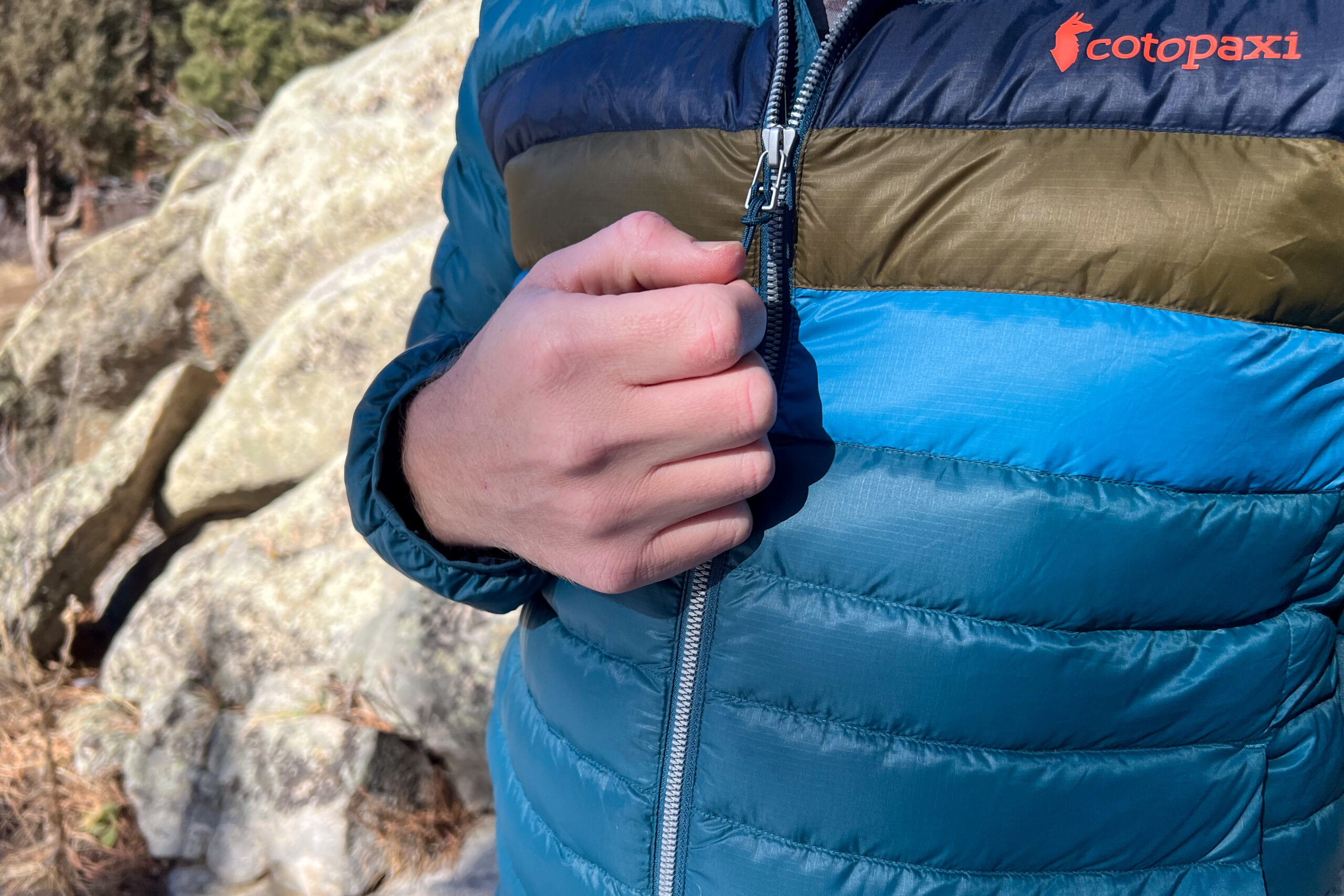 A person zipping up the Cotopaxi Fuego Down Jacket, highlighting the smooth front zipper and color-blocked design.