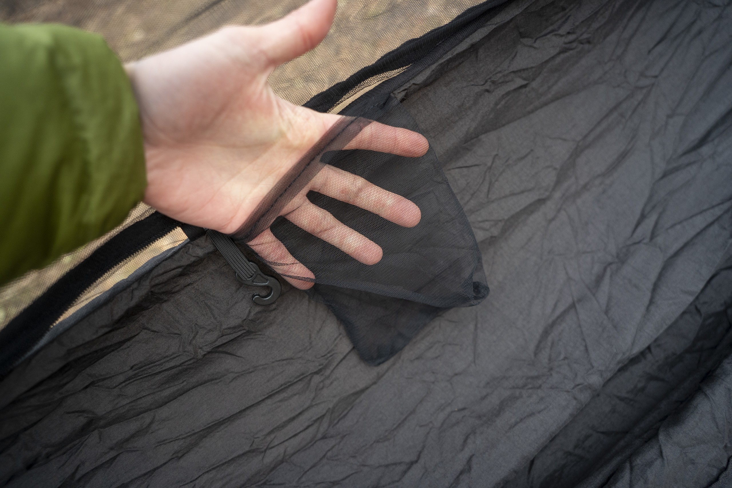 A hand extends into a mesh pocket on the side of a hammock