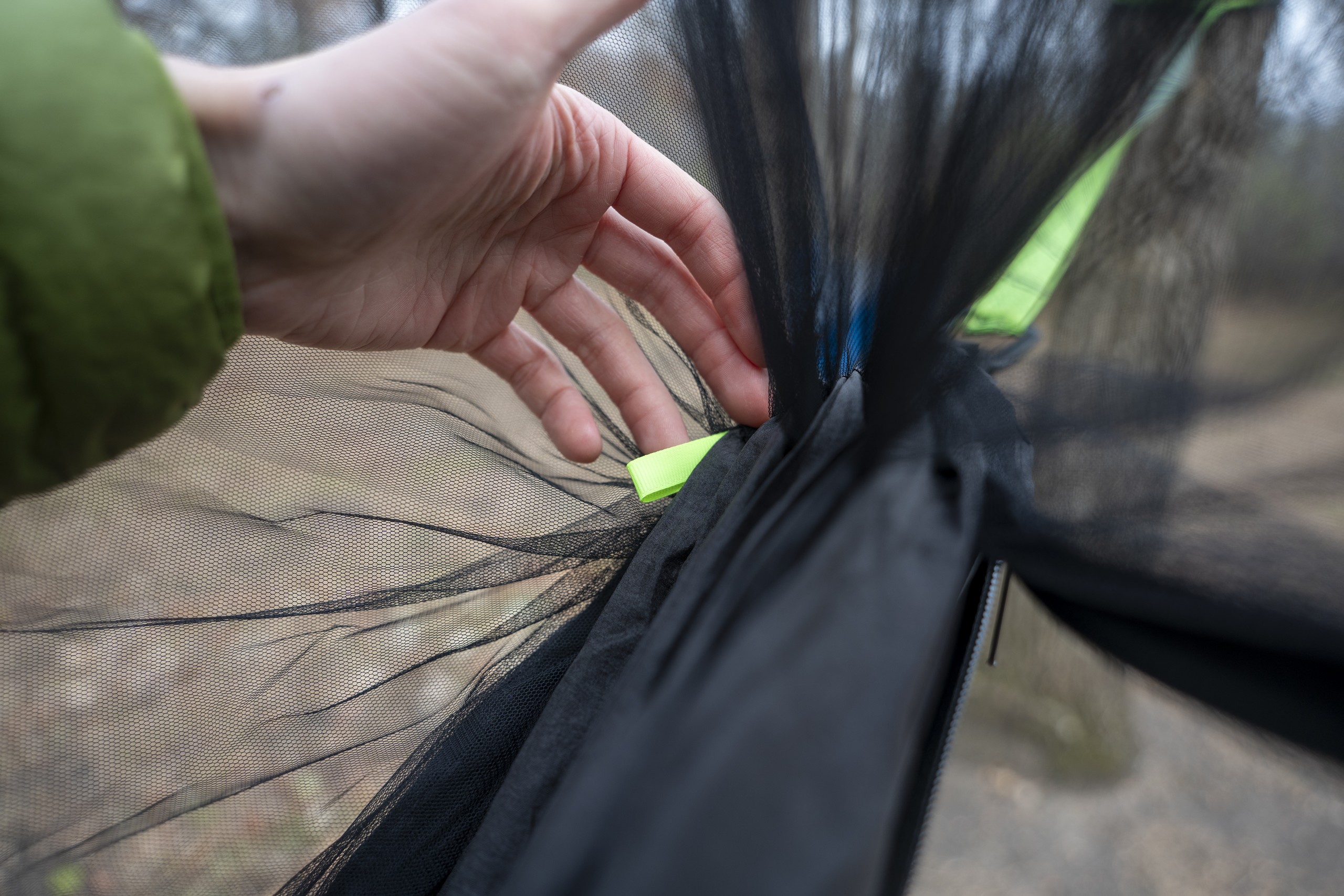 a hand holds a small green loop of fabric at the end of a hammock