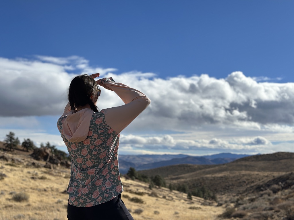 Woman in floral sun shirt looking out at view of foothills in high desert detting