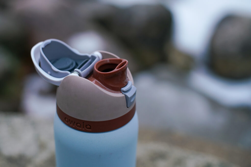 A close up of the Owala FreeSip Vacuum Insulated's spout with rocks in the background.