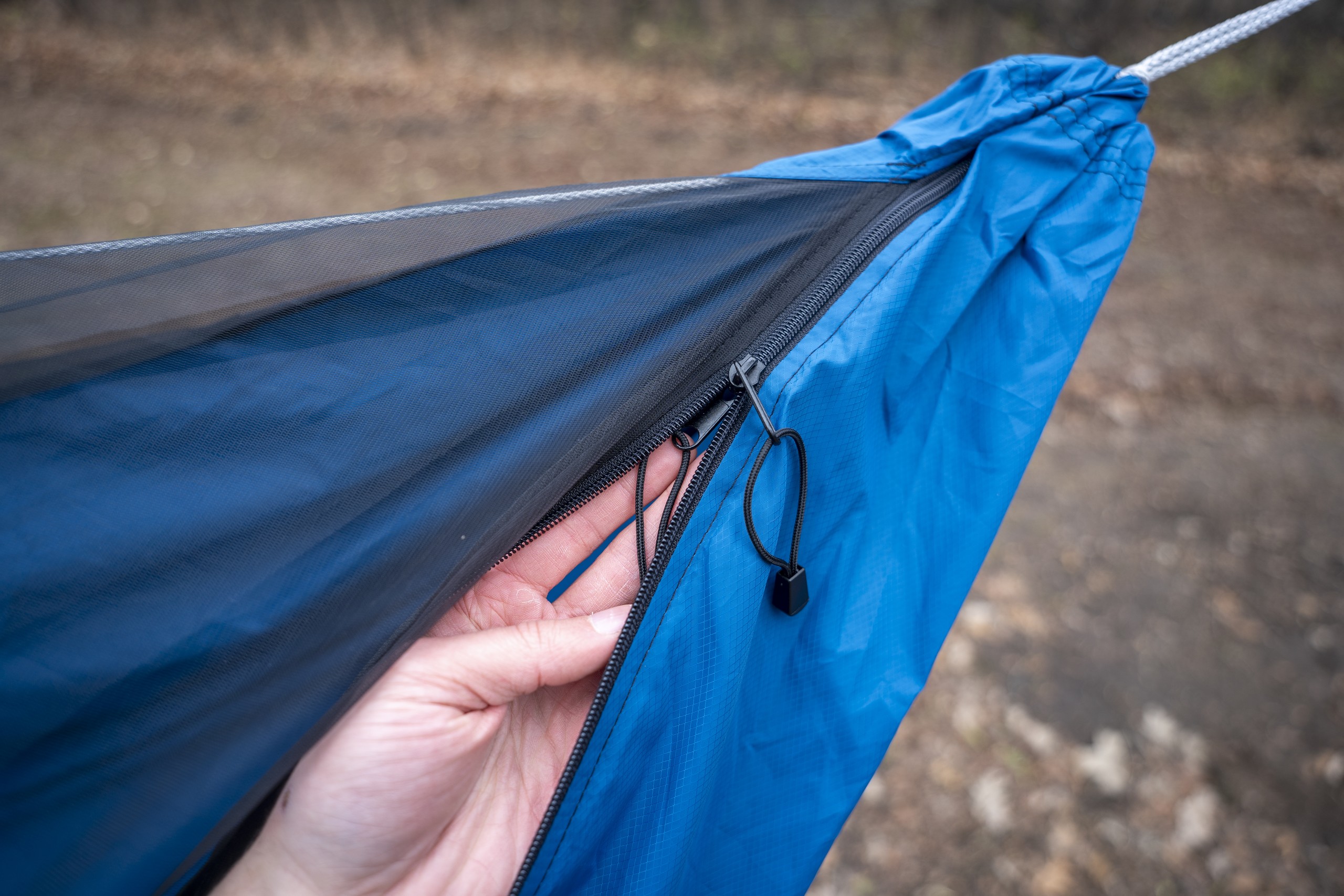 A hand holds open a hammock zipper