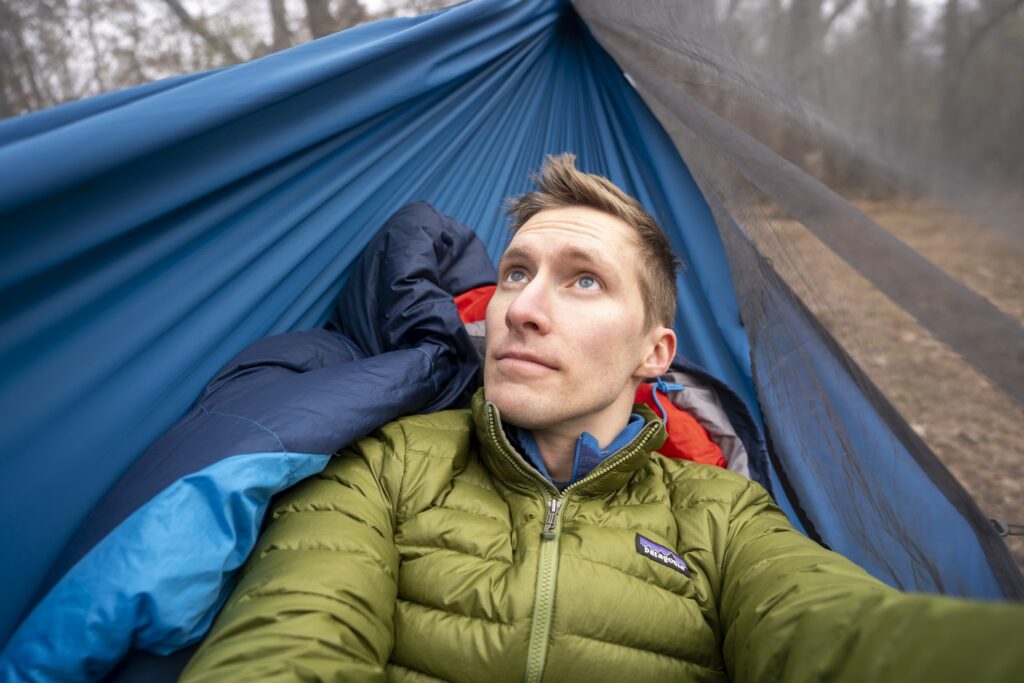 a man lays in a blue hammock from a selfie perspective