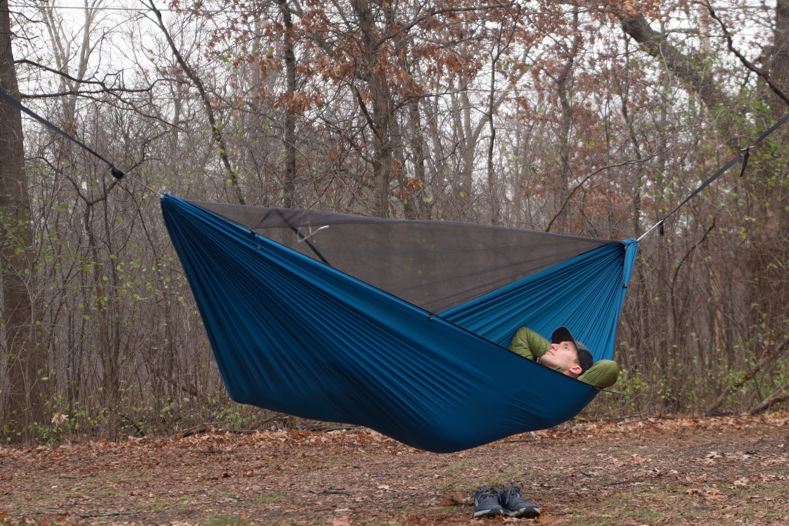 a man lays in a blue hammock in a clearing in the forest