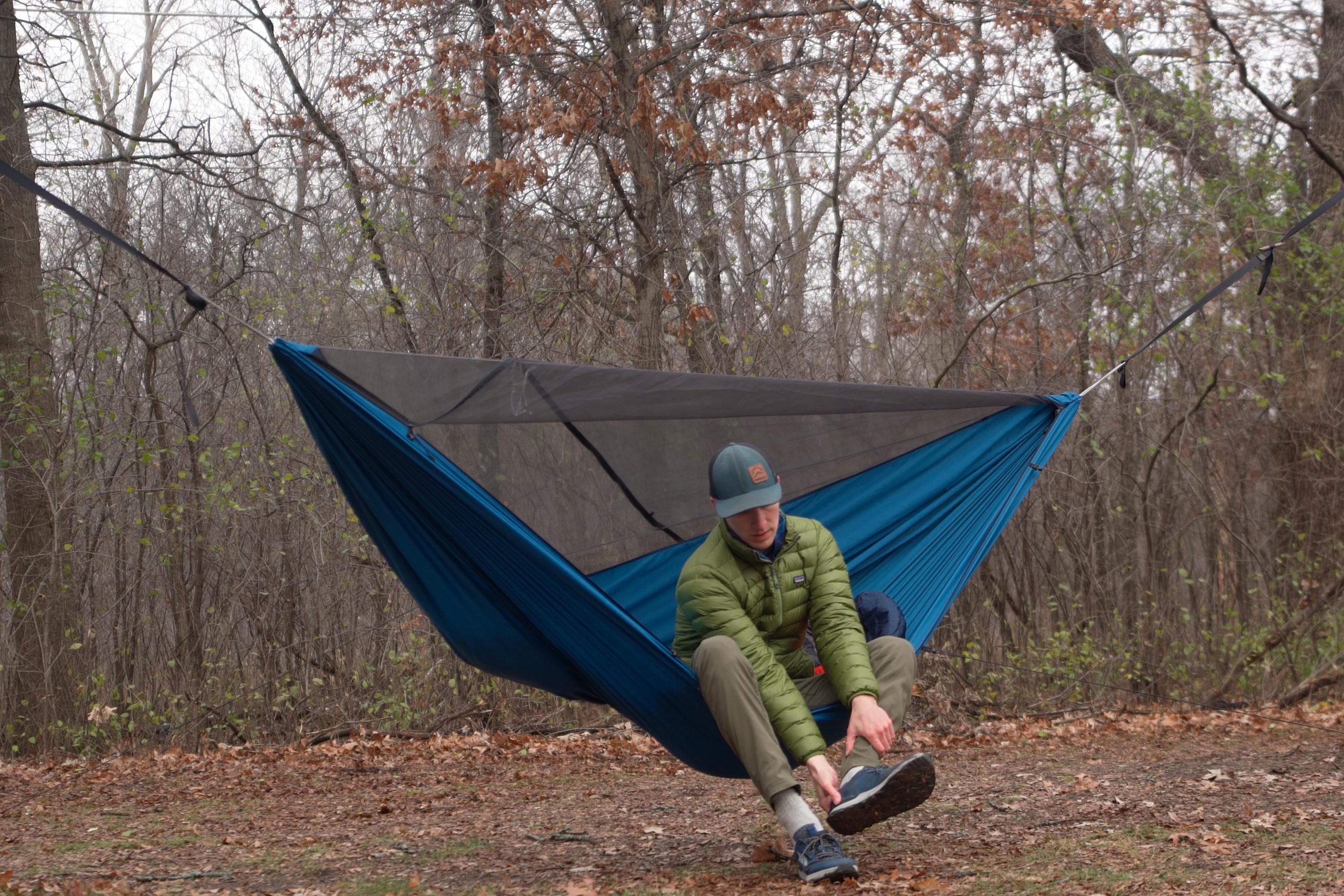 A man in a green jacket sits in a blue hammock