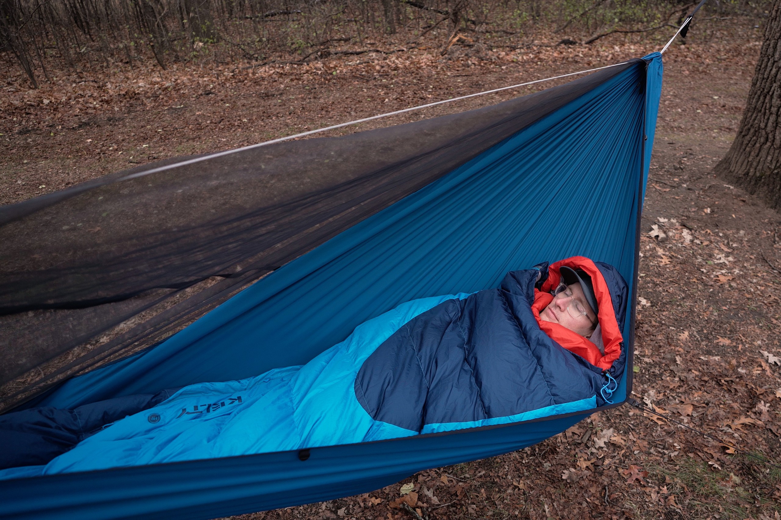 a man in a blue sleeping bag lays in a blue hammock