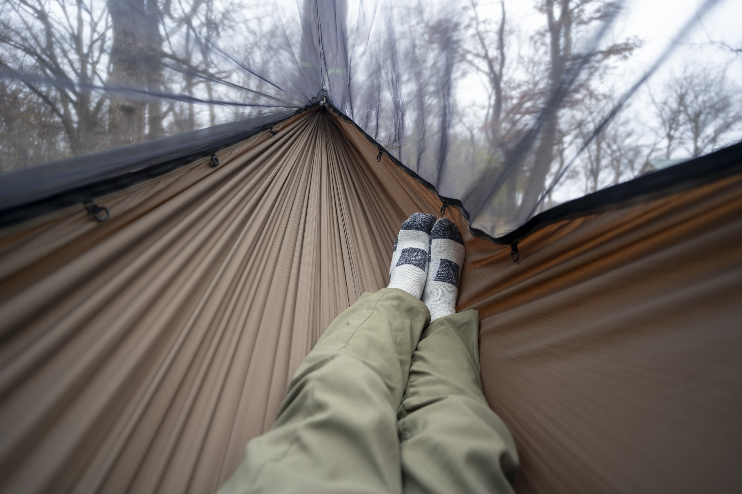 a pair of legs extends into a green hammock from a point of view perspective