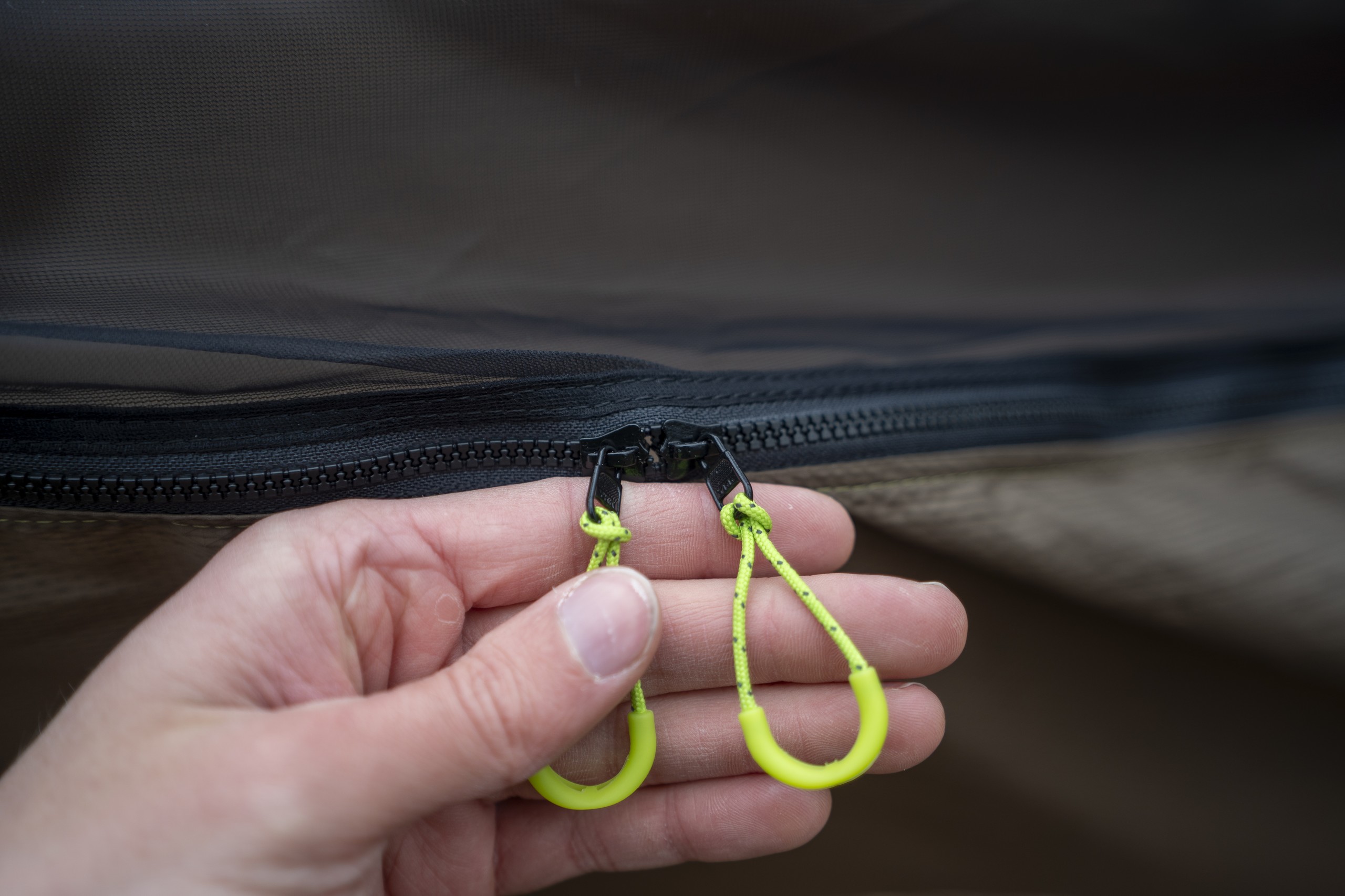 a hand holds two green loop zipper pulls