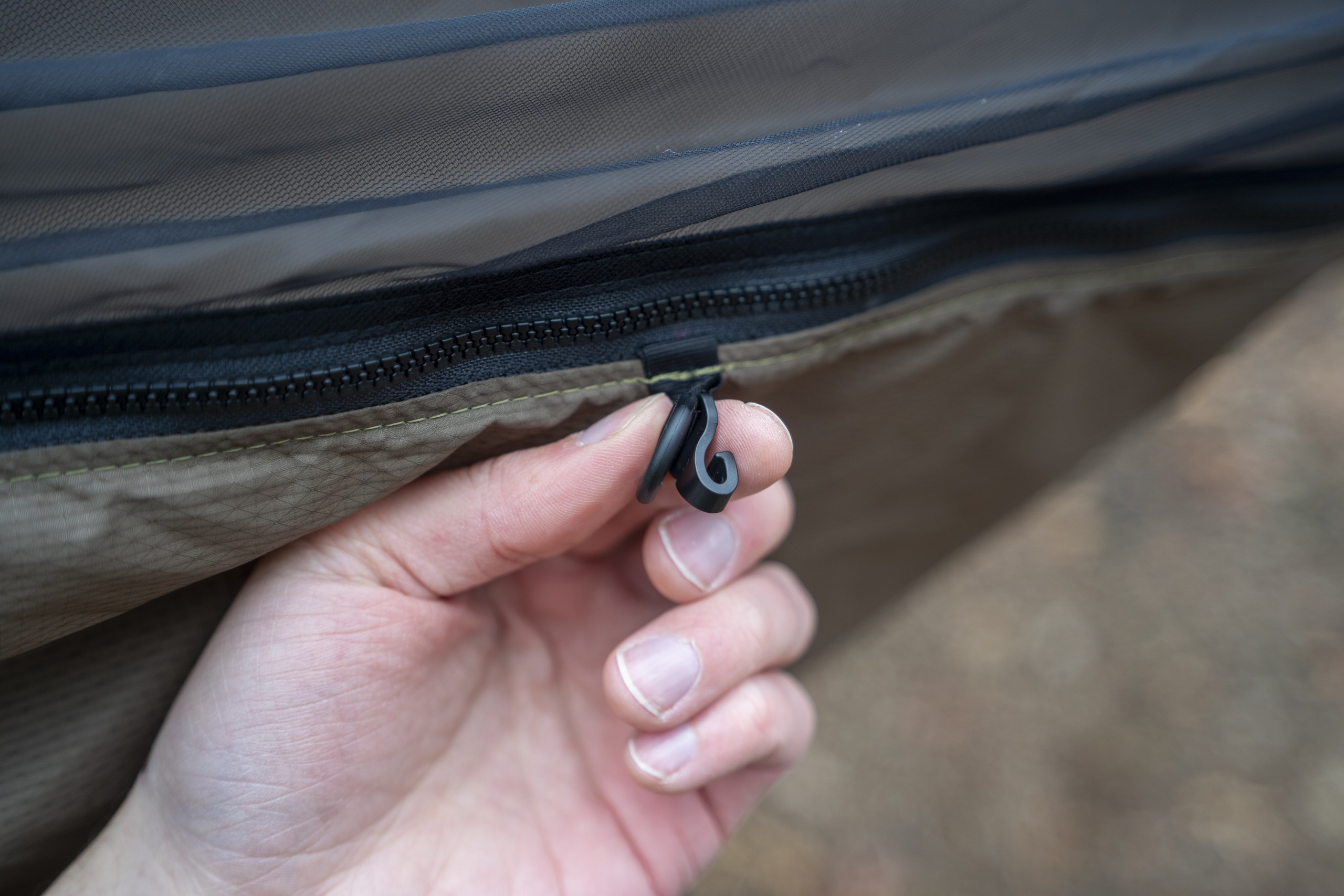 a hand holds a small hook on the side of a hammock