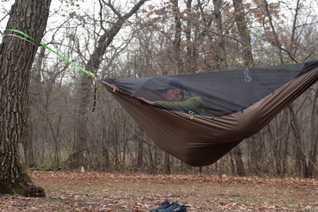 a green hammock hangs in a forest clearing