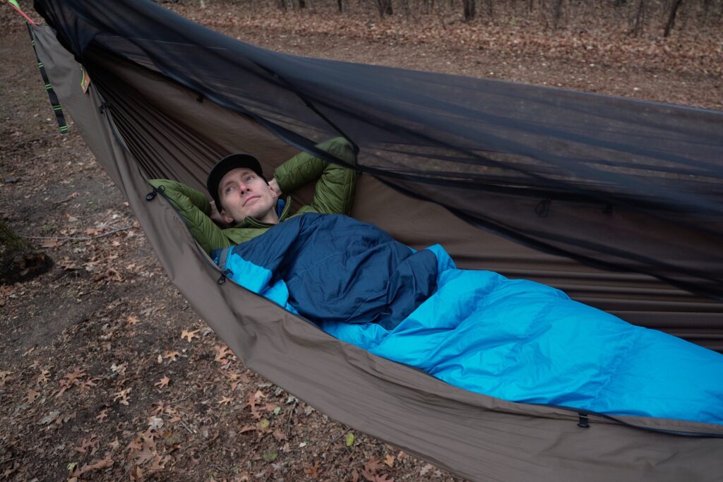 a man in a blue sleeping bad lays in a green hammock