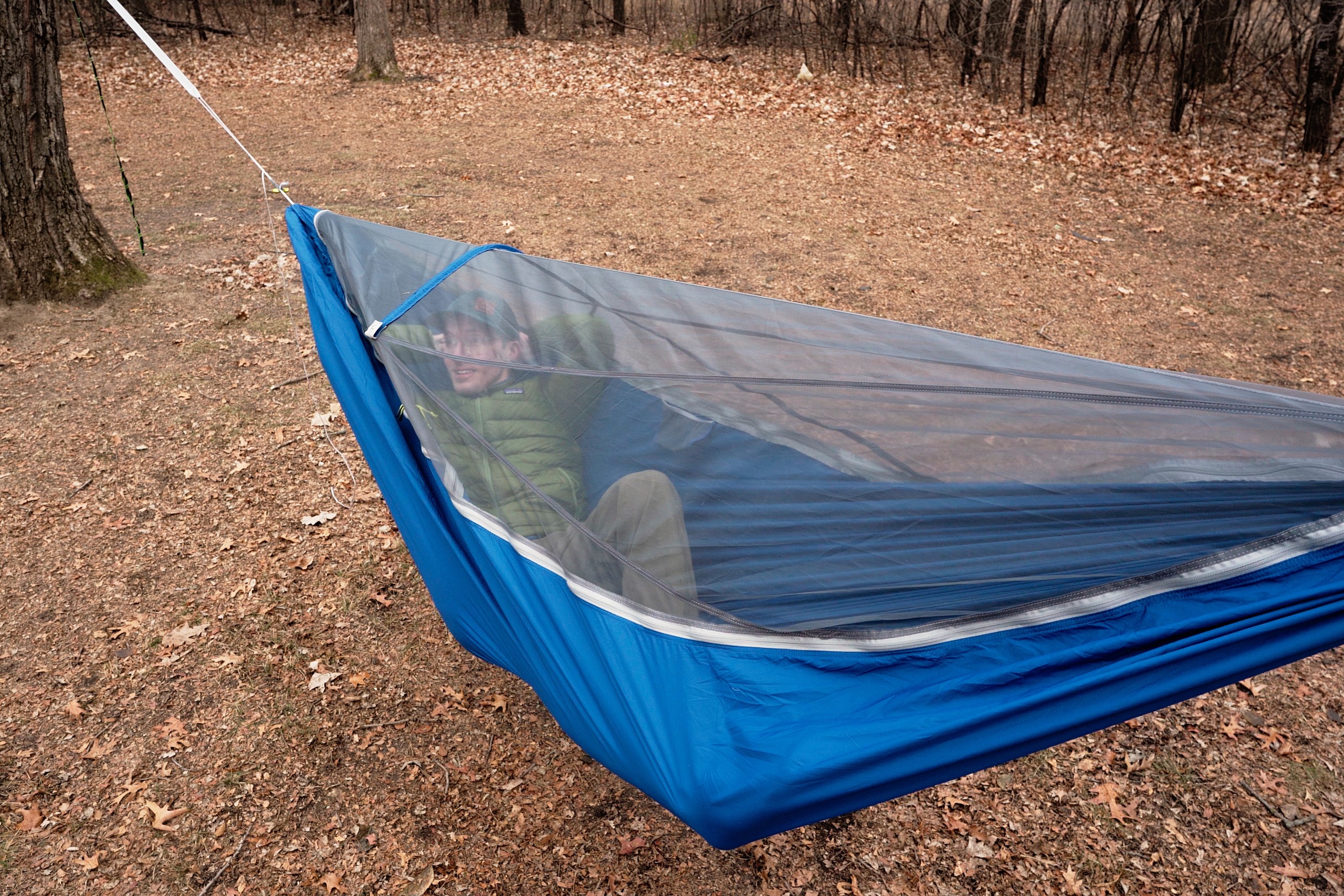 a man reclines in a blue hammock with a bug net