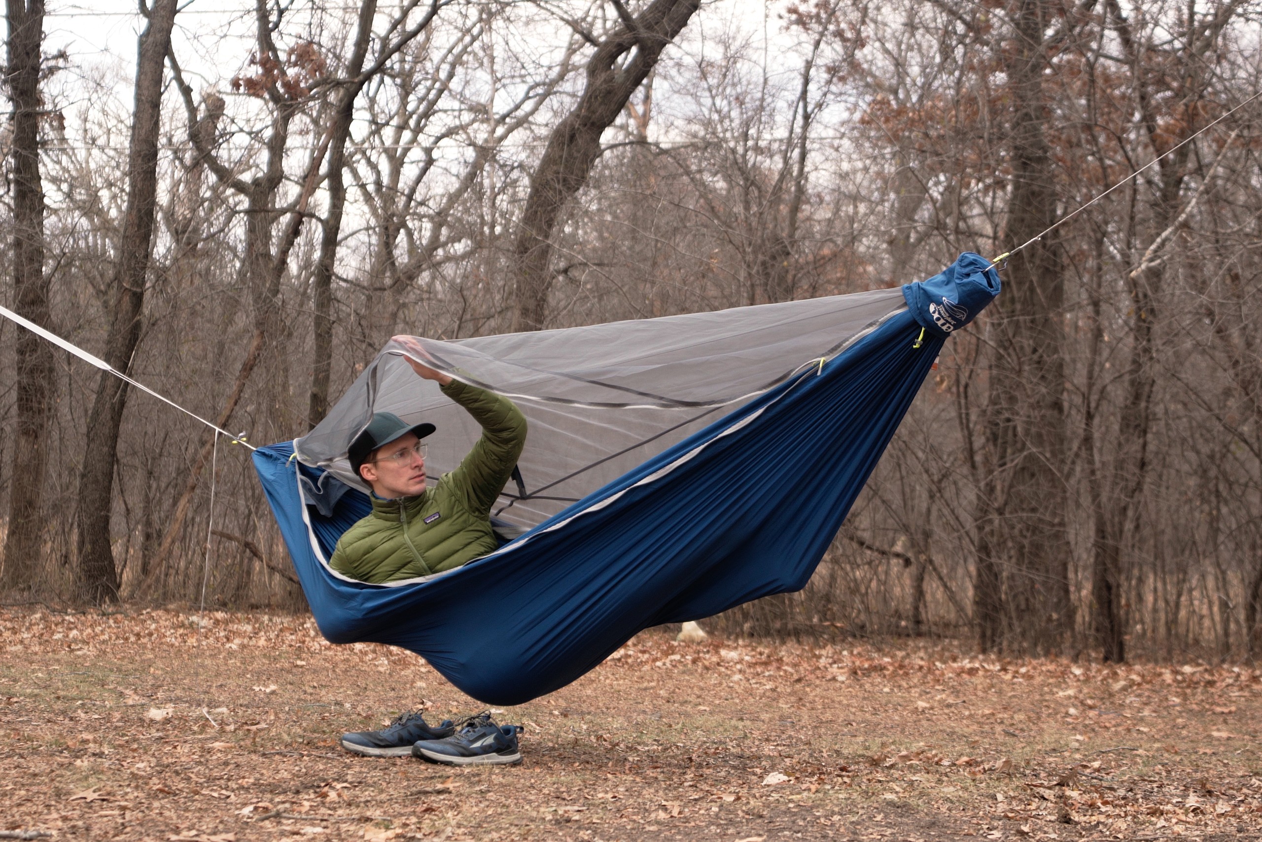 a man in a green jacket sits in a blue hammock