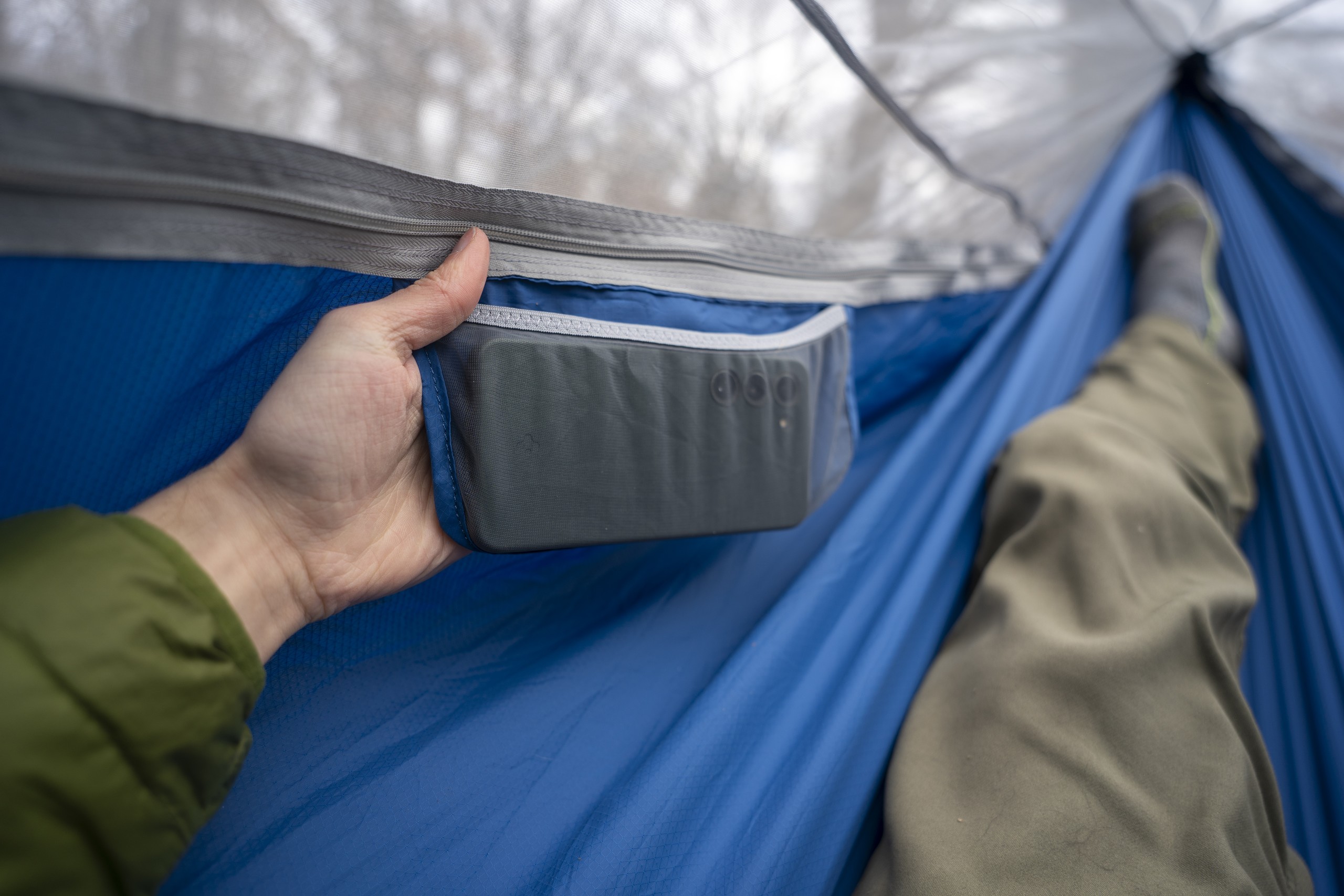 a hand holds a side pocket on a hammock holding a phone