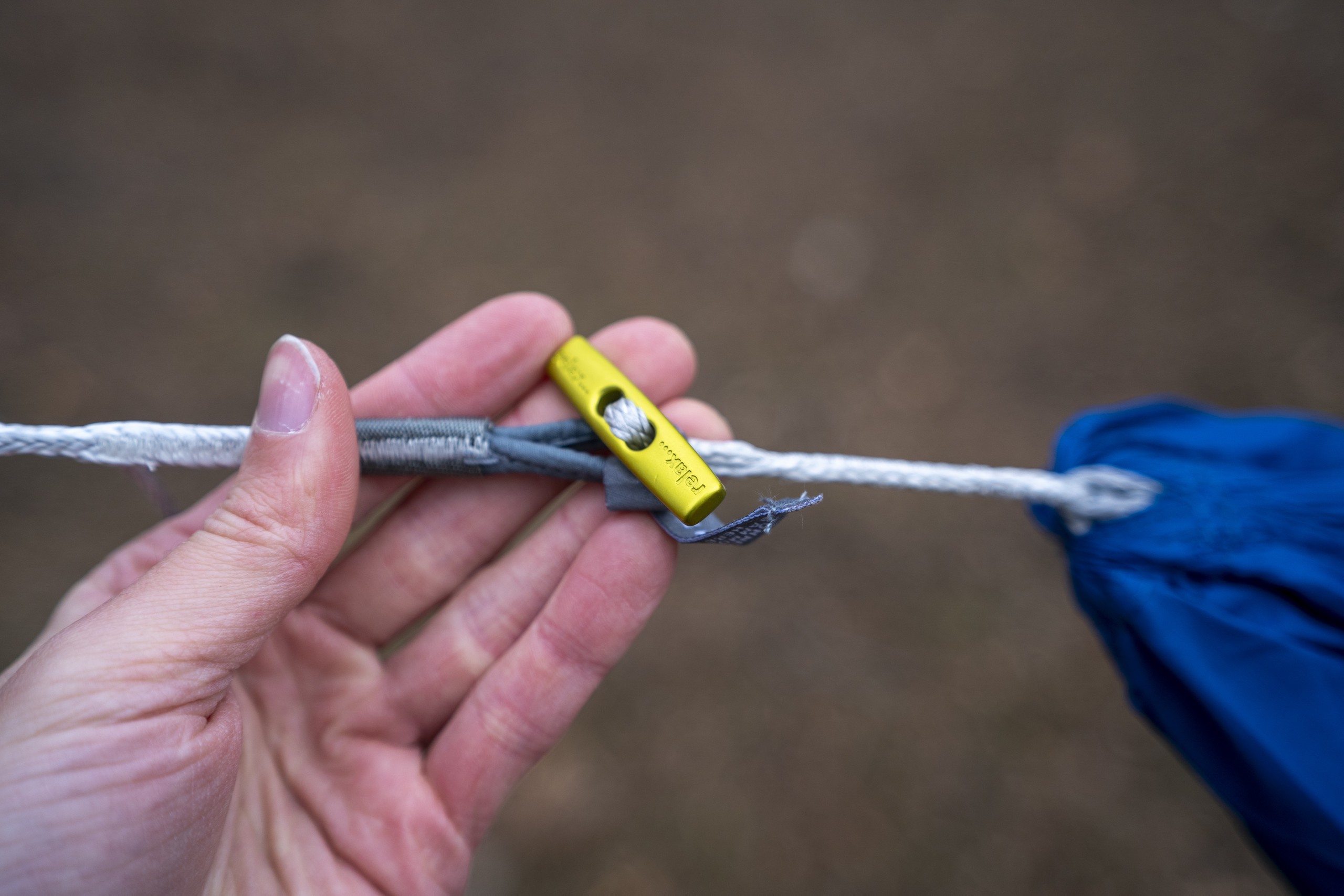 a hand holds a metal toggle on the end of a hammock suspension