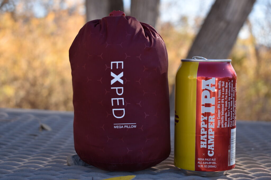 The packed Exped Mega Pillow rests next to a smaller 12 oz can of Happy Camper IPA for a size comparison