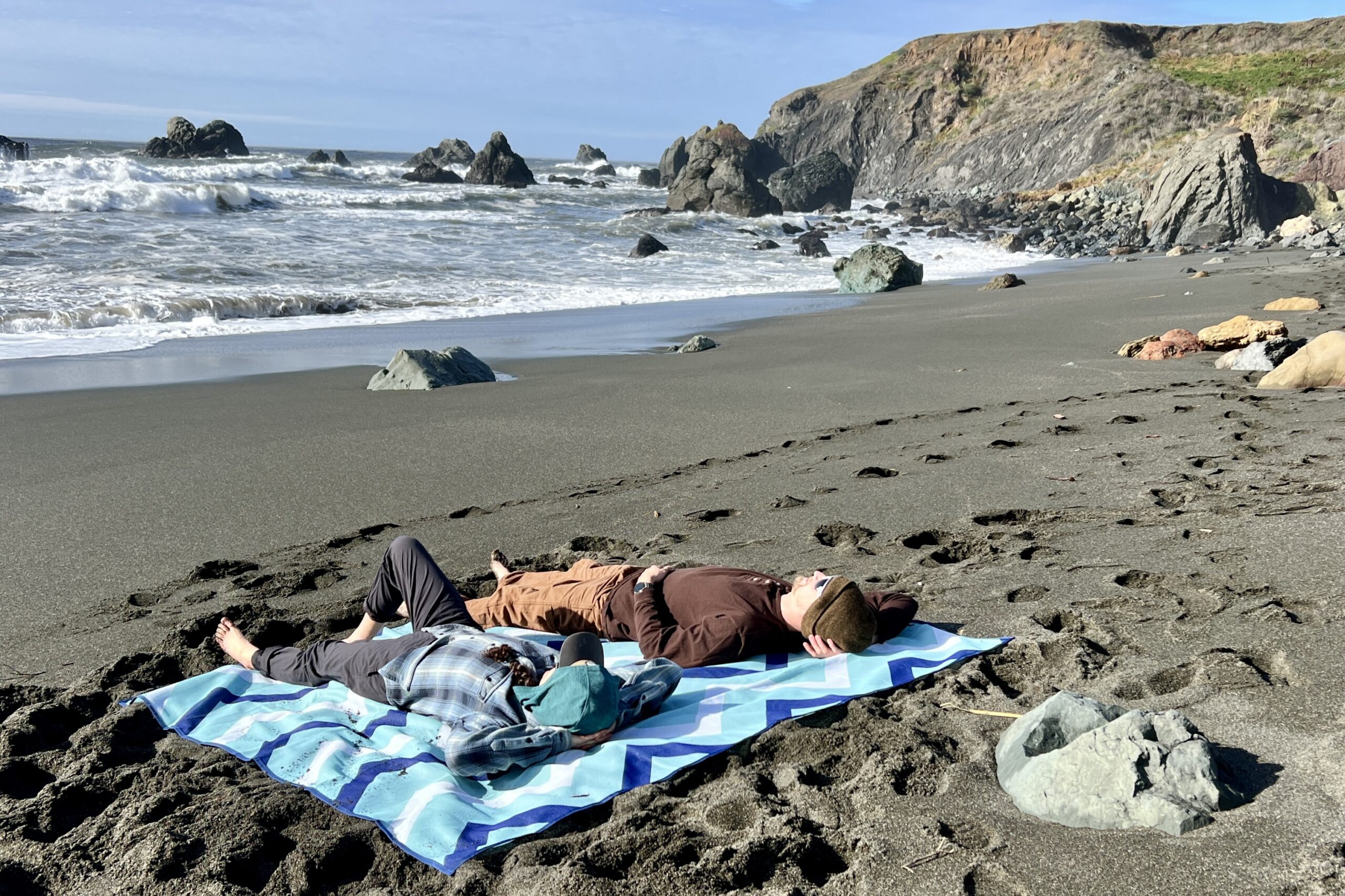 2 people laying on the CGear Multimats Sandlite Sand-free Mat in the San direction at the beach.