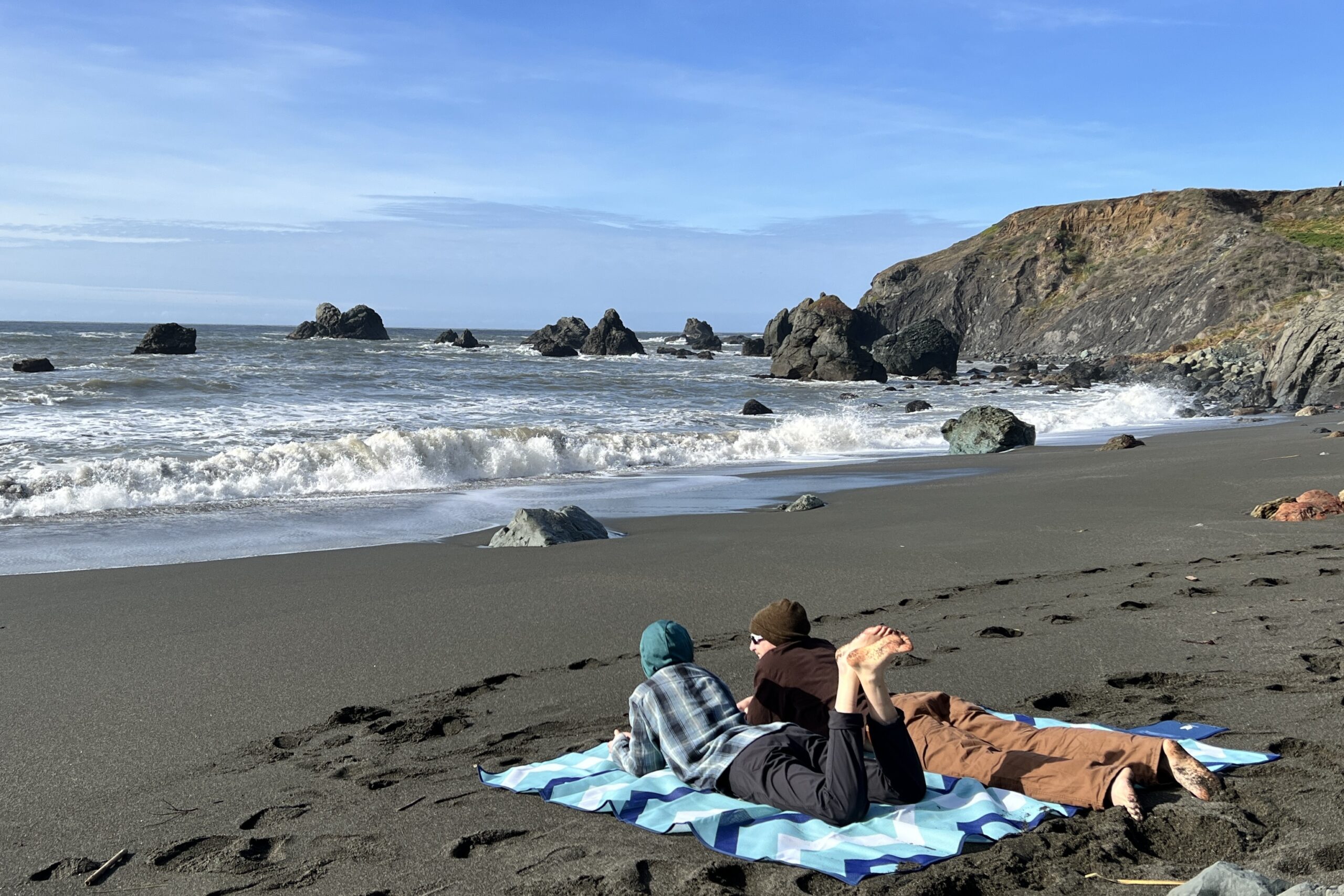 2 people lay in on their stomaches on the large size of the CGear Multimats Sandlite Sand-free Mat at the beach.