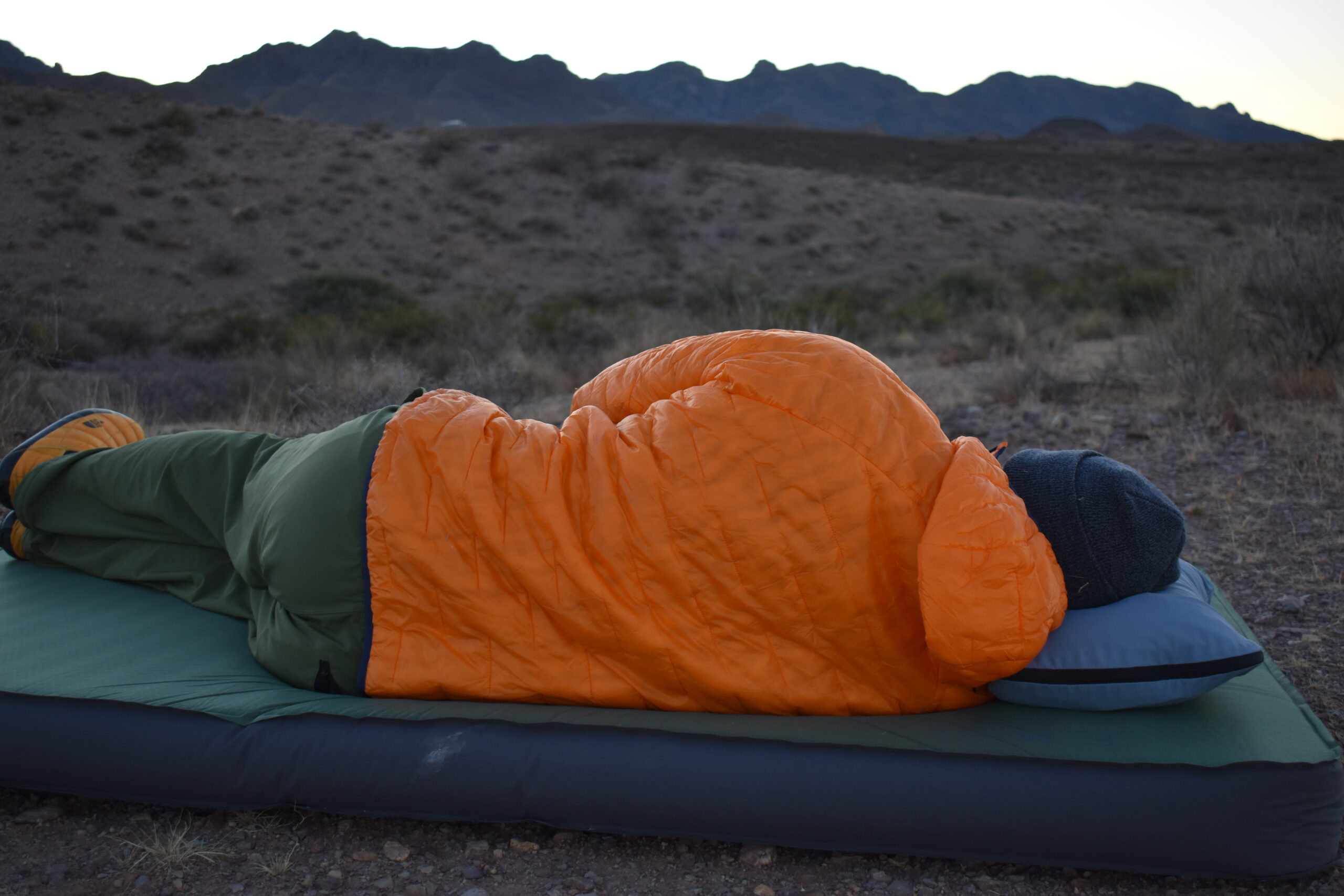 Hiker laying on his side while sleeping on the HEST Camp Pillow and facing the mountains just before sunrise