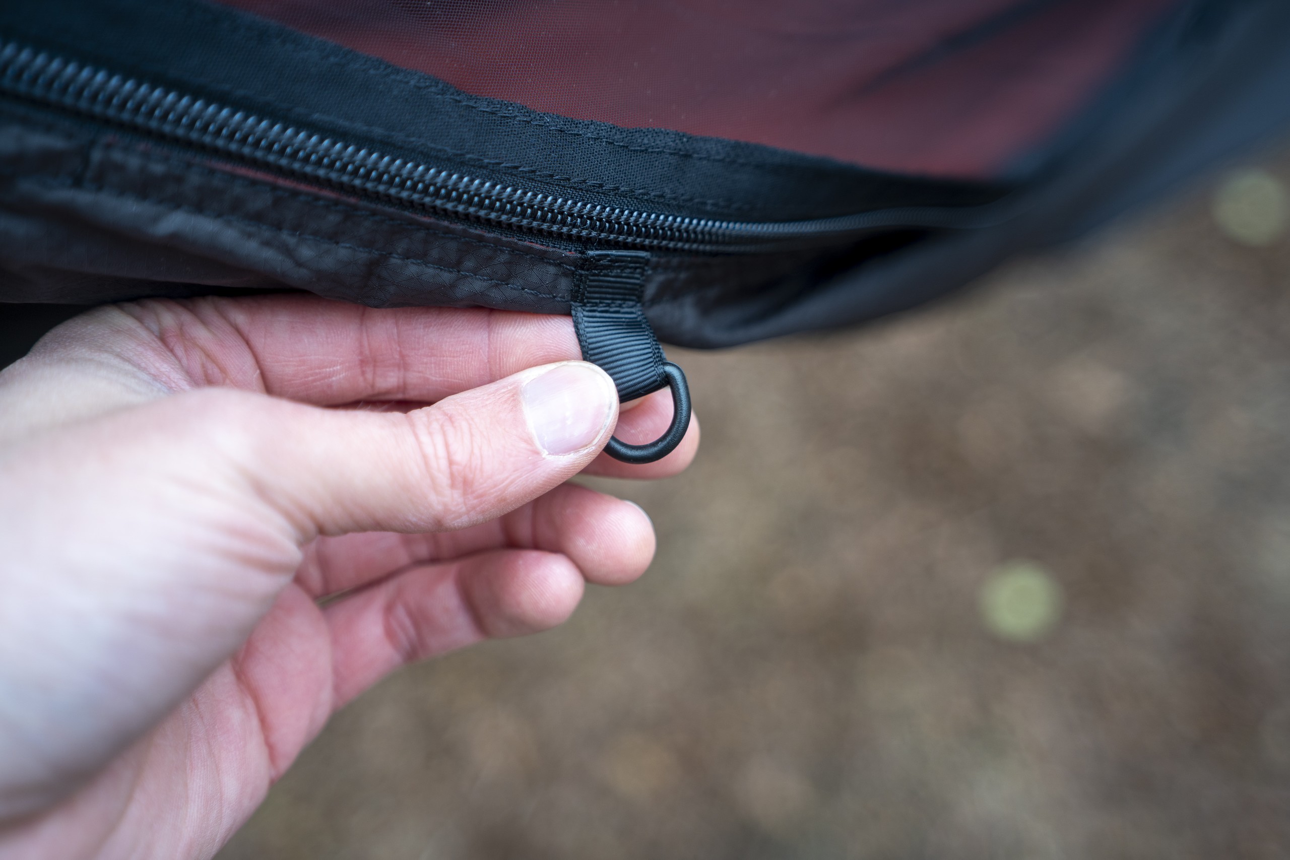 a hand holds a d ring on the exterior of a hammock