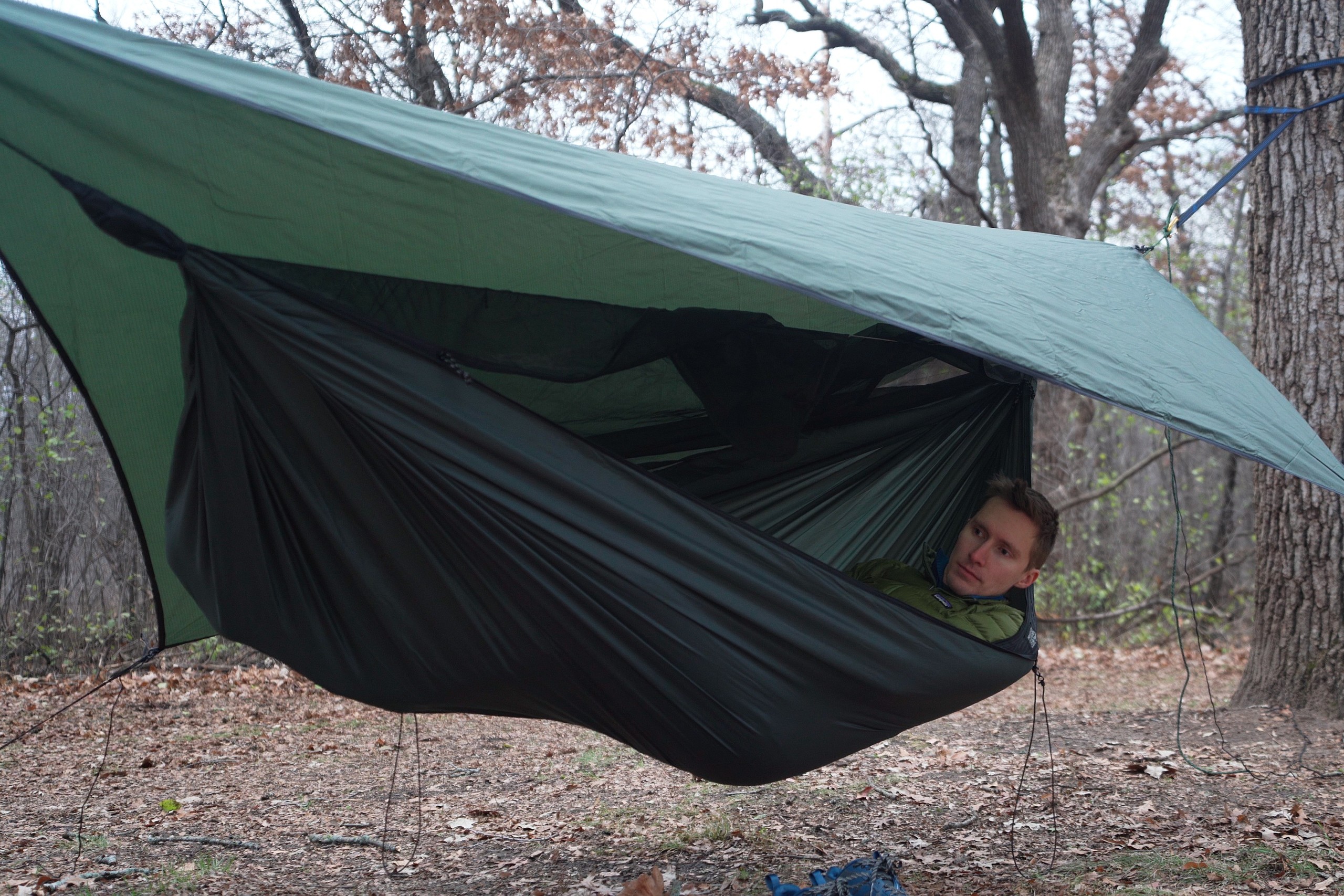 a man lays in a green hammock with a green tarp overhead