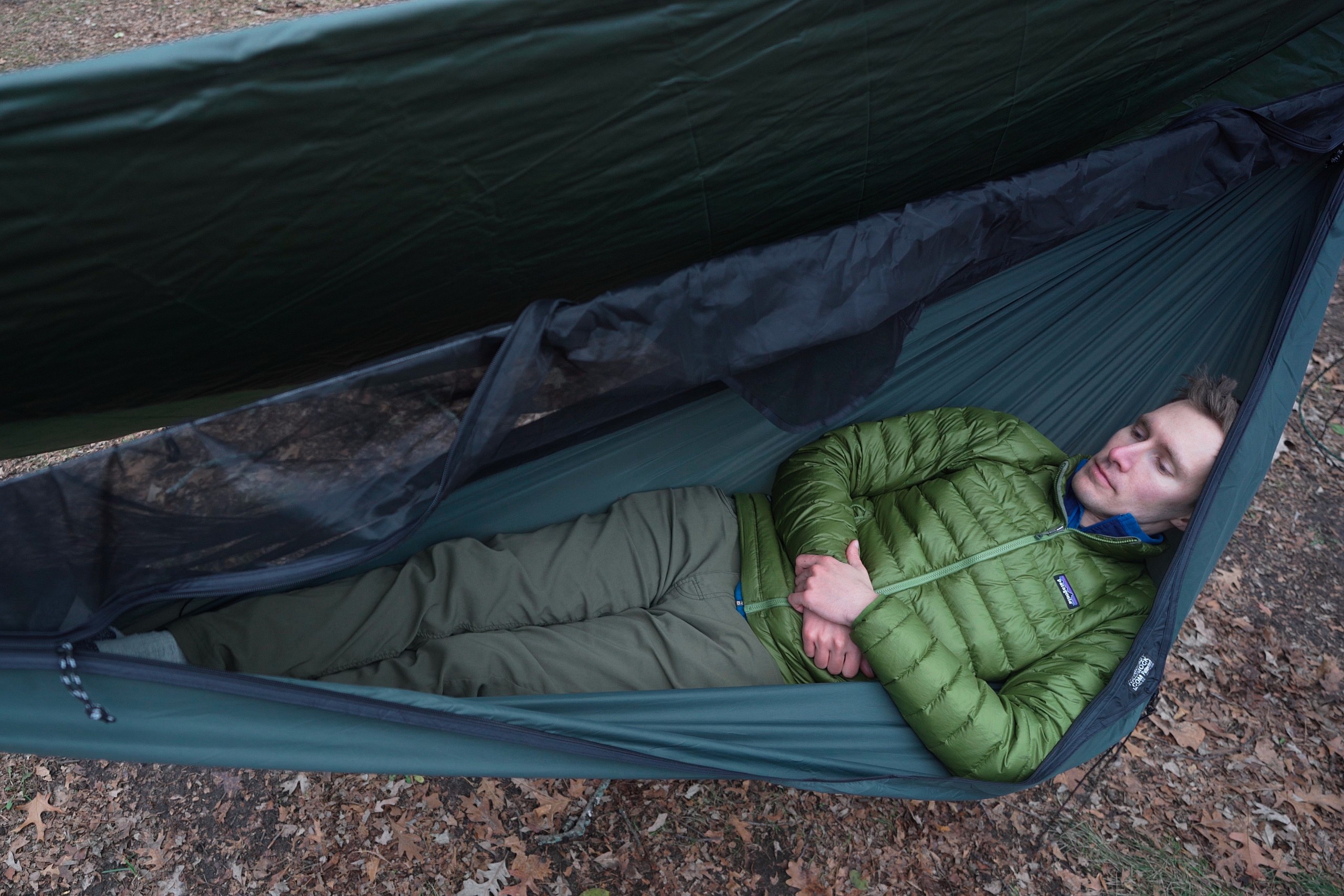 a man in a green jacket lies in green hammock