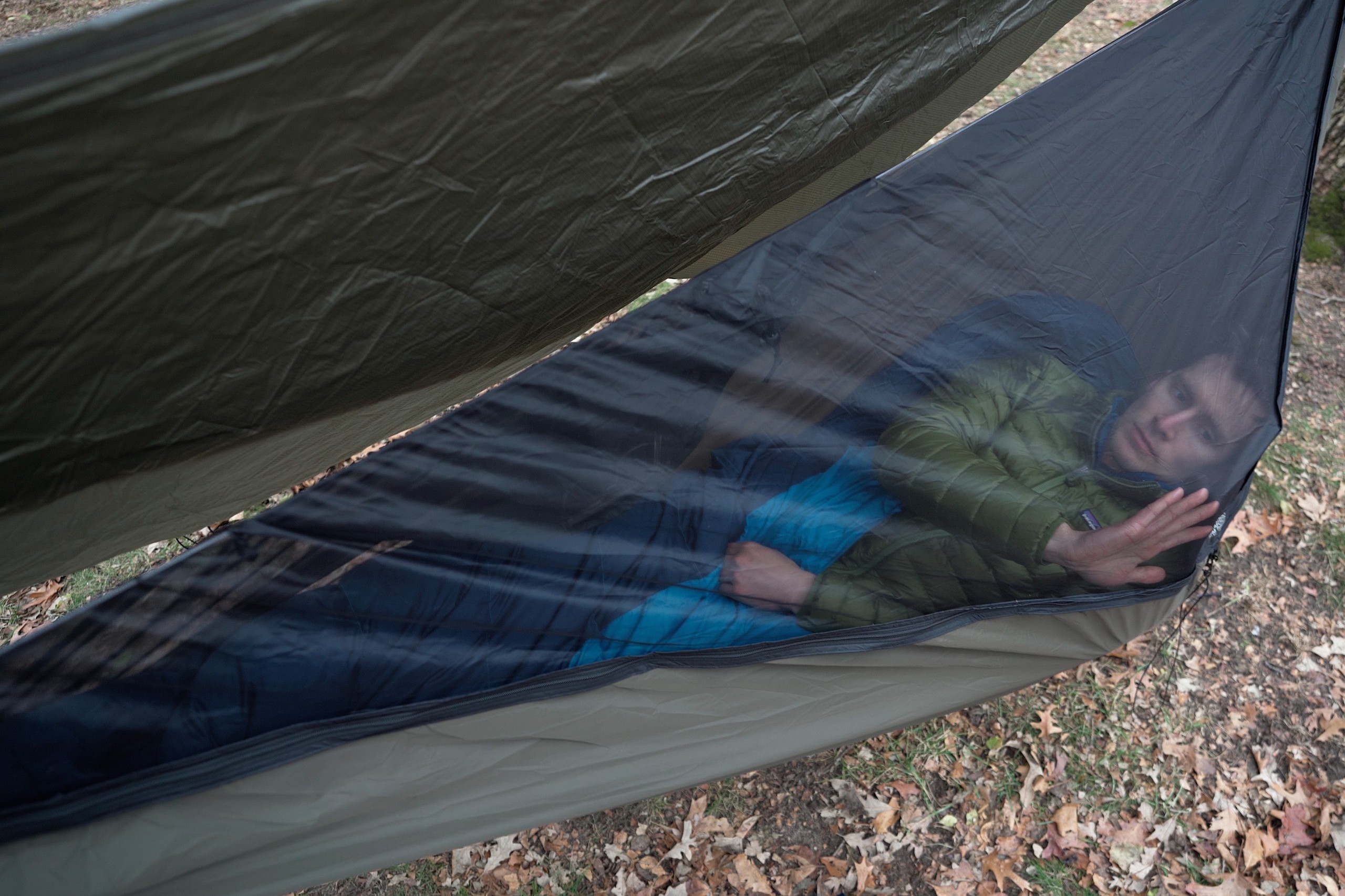 a man lies in a hammock with a bug net zipped over him