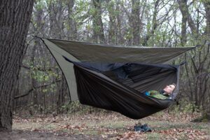 a man lies in a green hammock under a green tarp