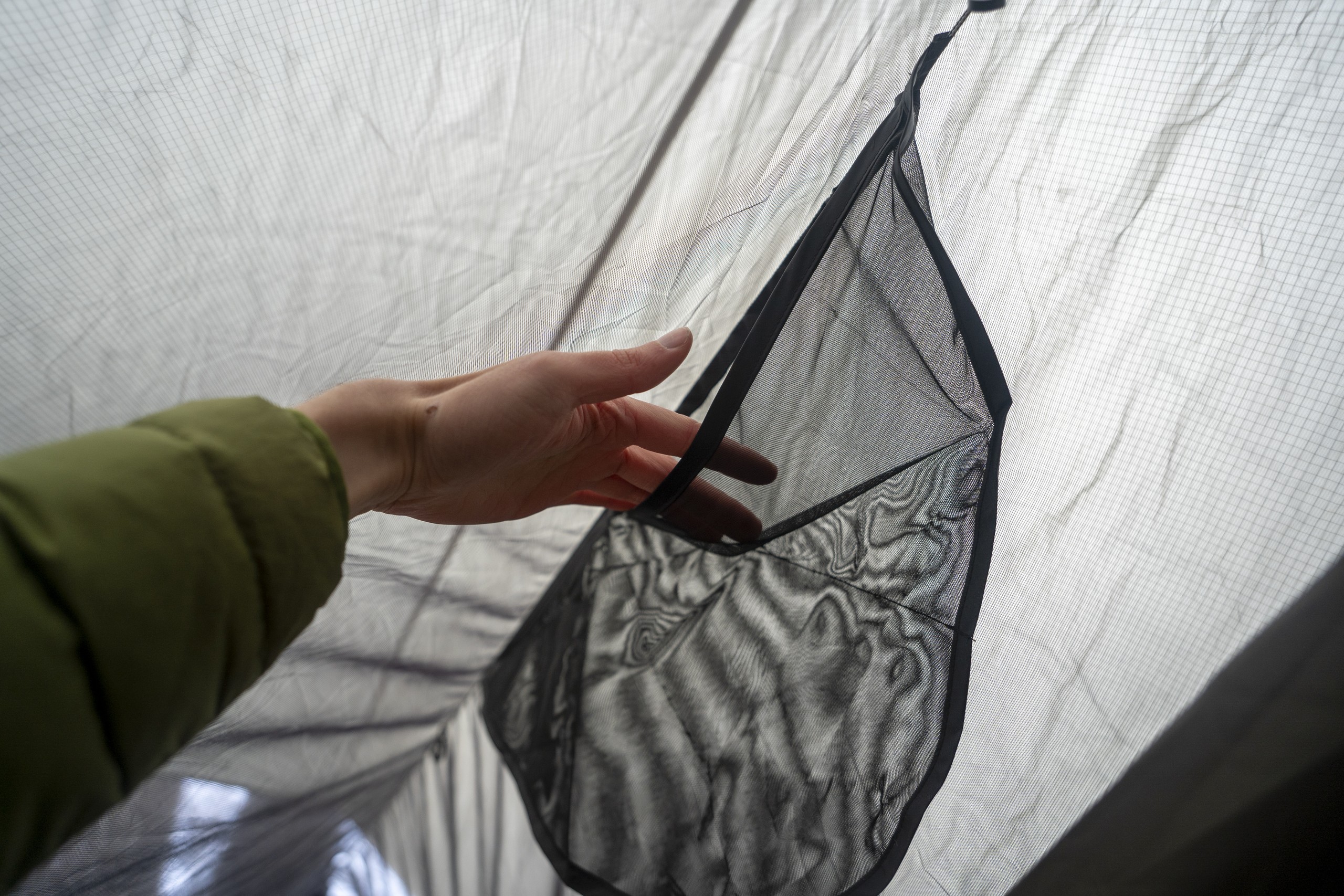 a hand holds open a pocket on a hammock ridgeline organizer