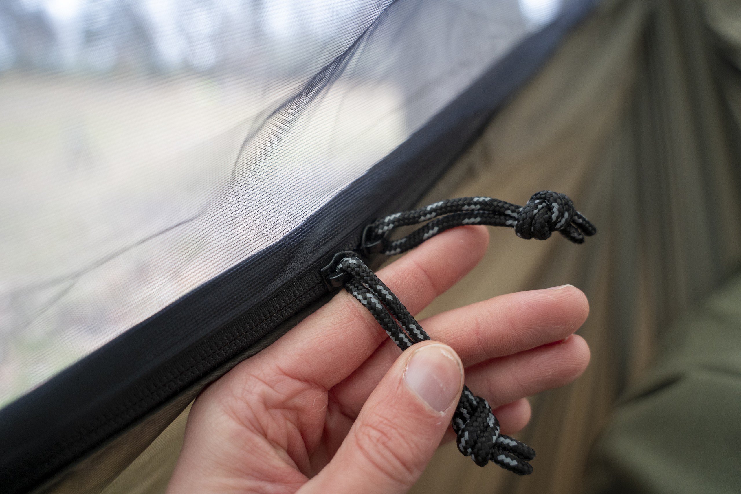 a hand holds cord zipper pulls on a hammock