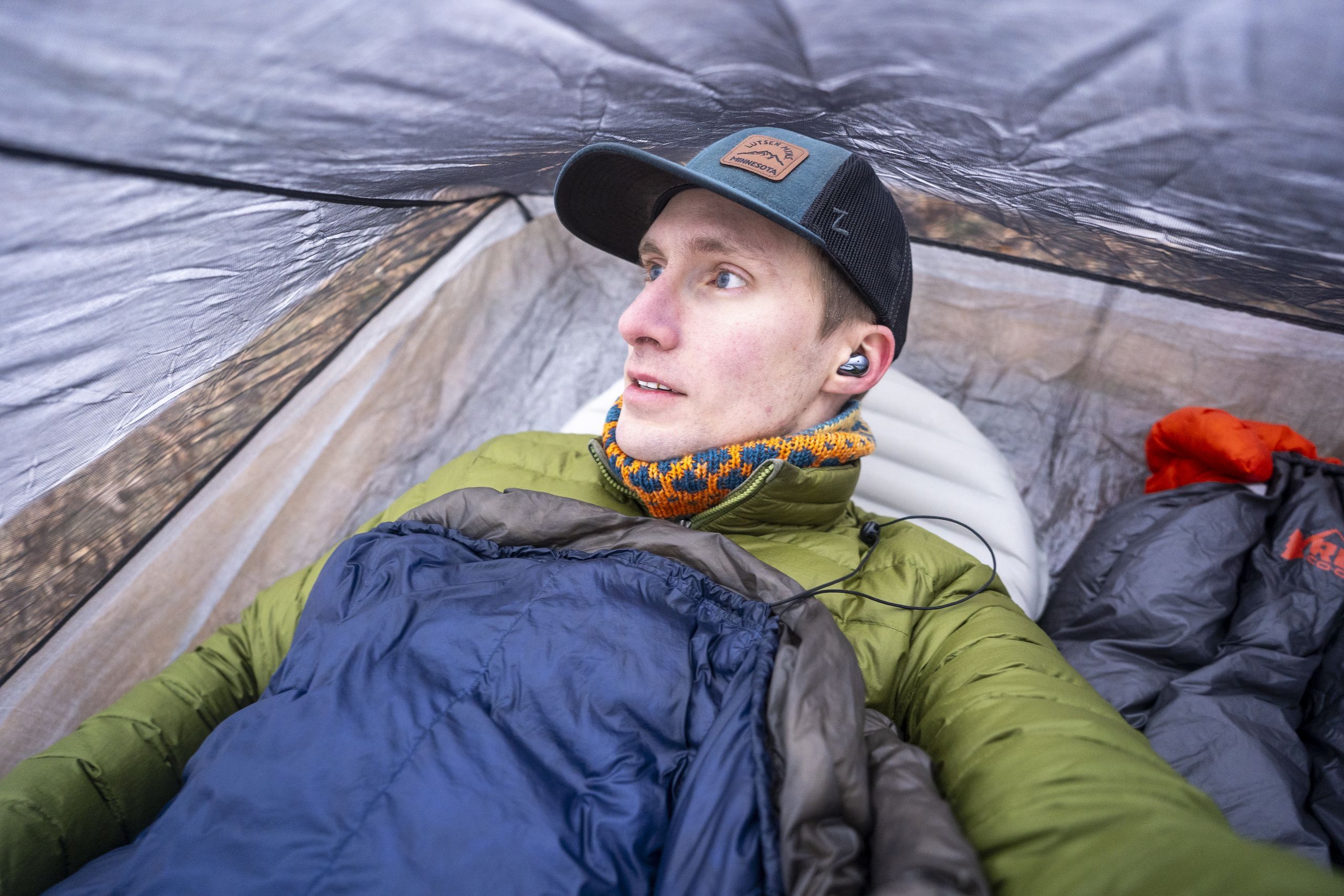 a man in a green coat lays in a tent