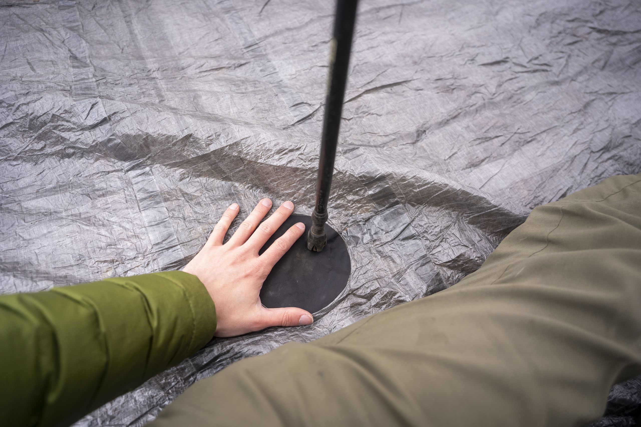 a hand rests on the floor of a tent with a trekking pole standing up