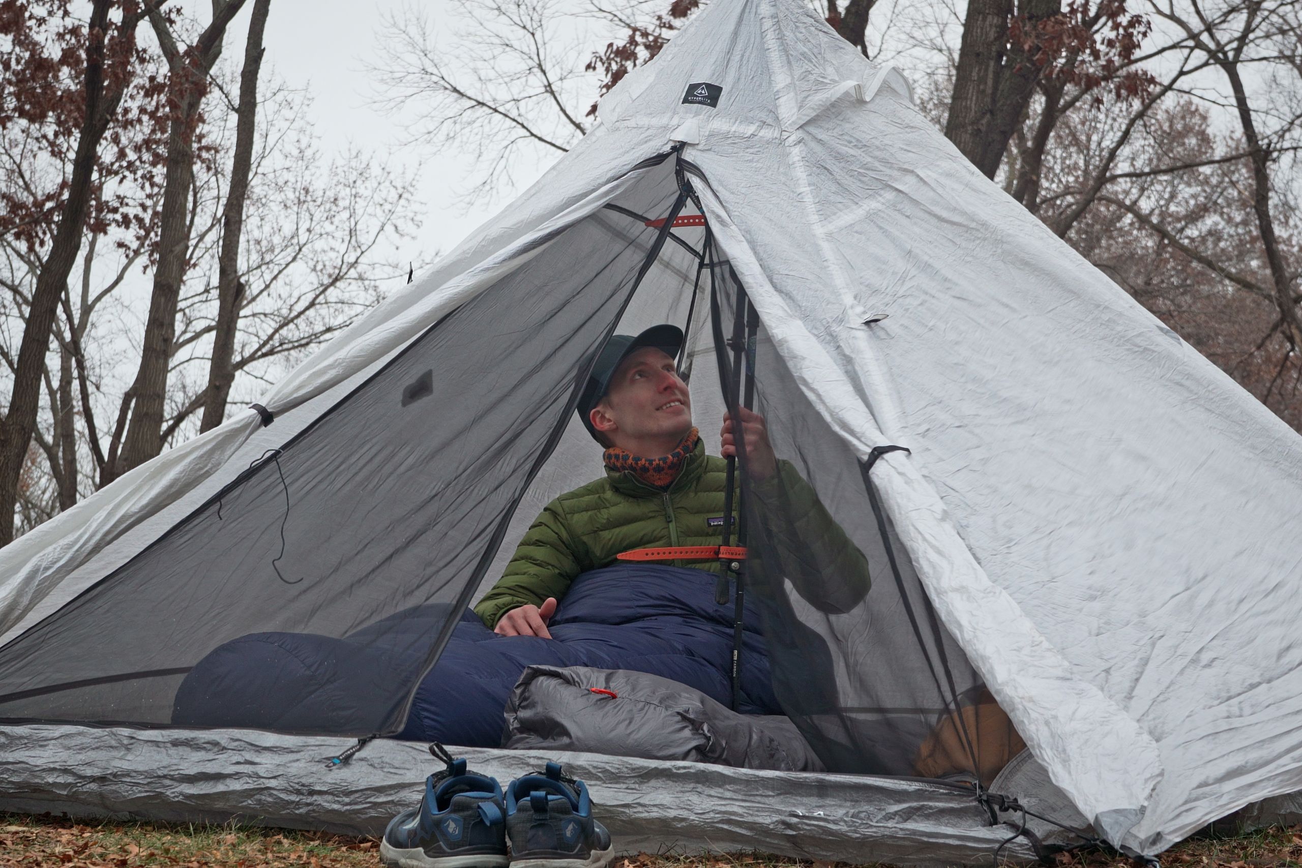 a man in a green coat sits up in a white pyramid tent