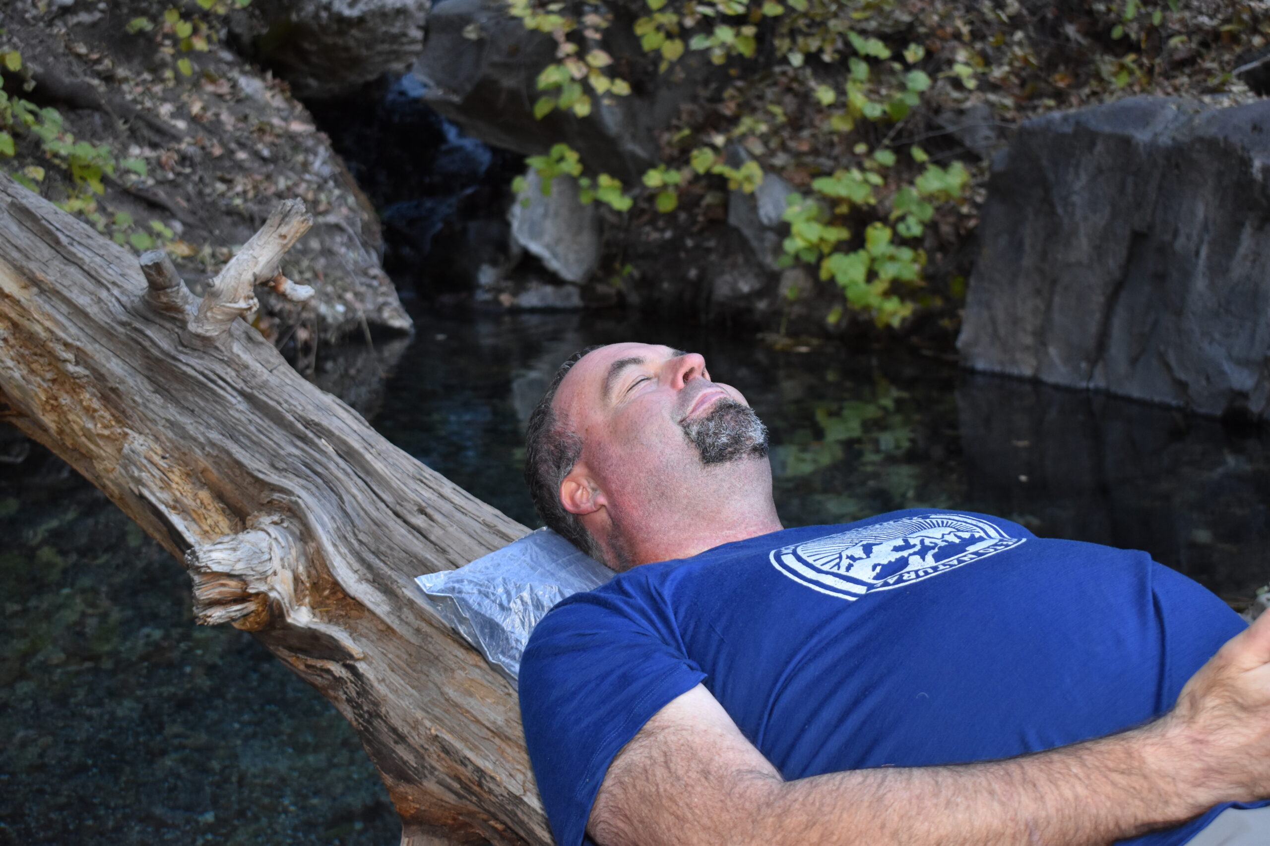 A male backpacker rests on the Hyperlite Stuff Sack Pillow next to a hot spring