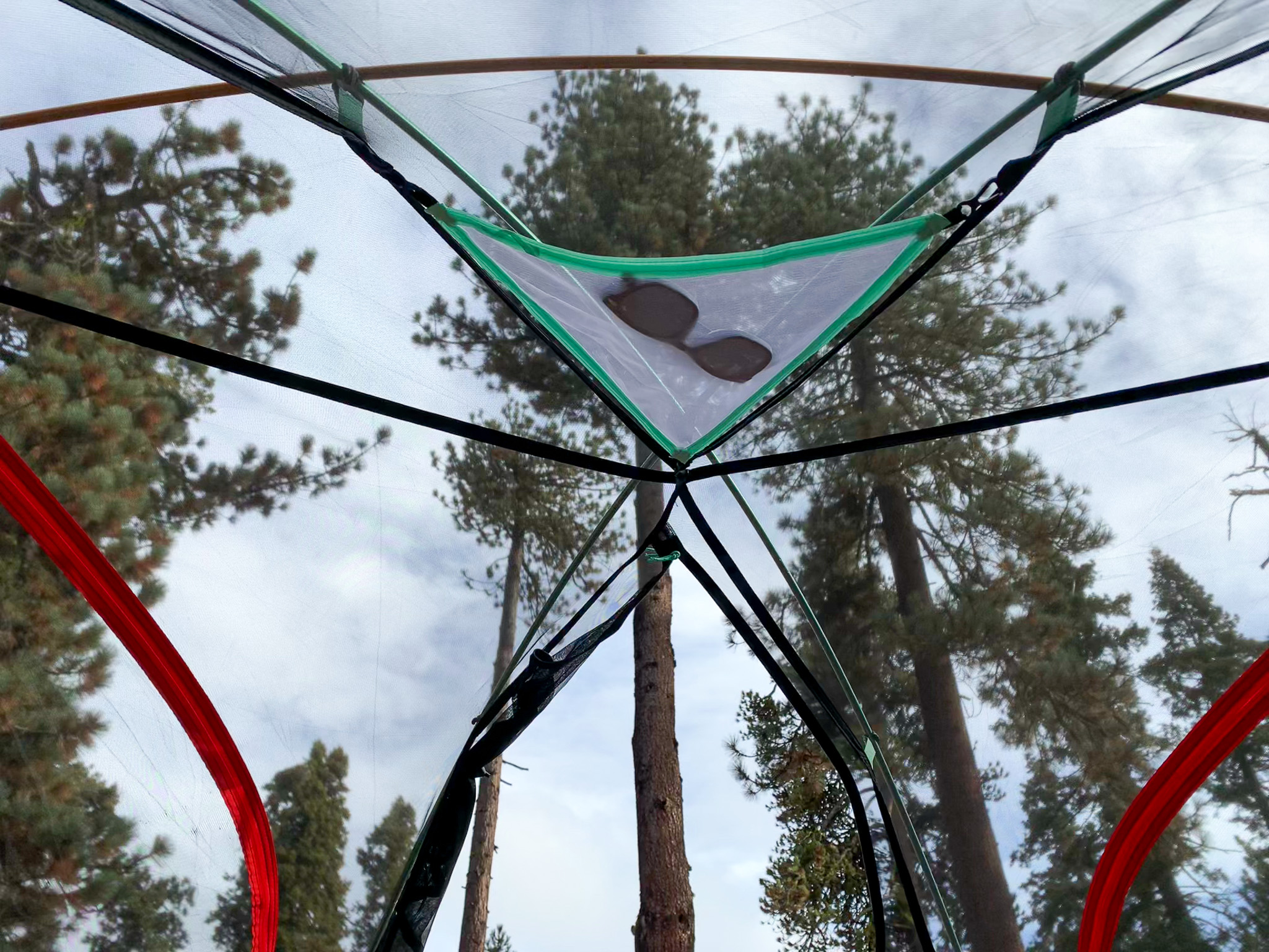 View looking upwards at the removable gear loft with a pair of sunglasses in it. The sky and pine trees visible through the mesh.