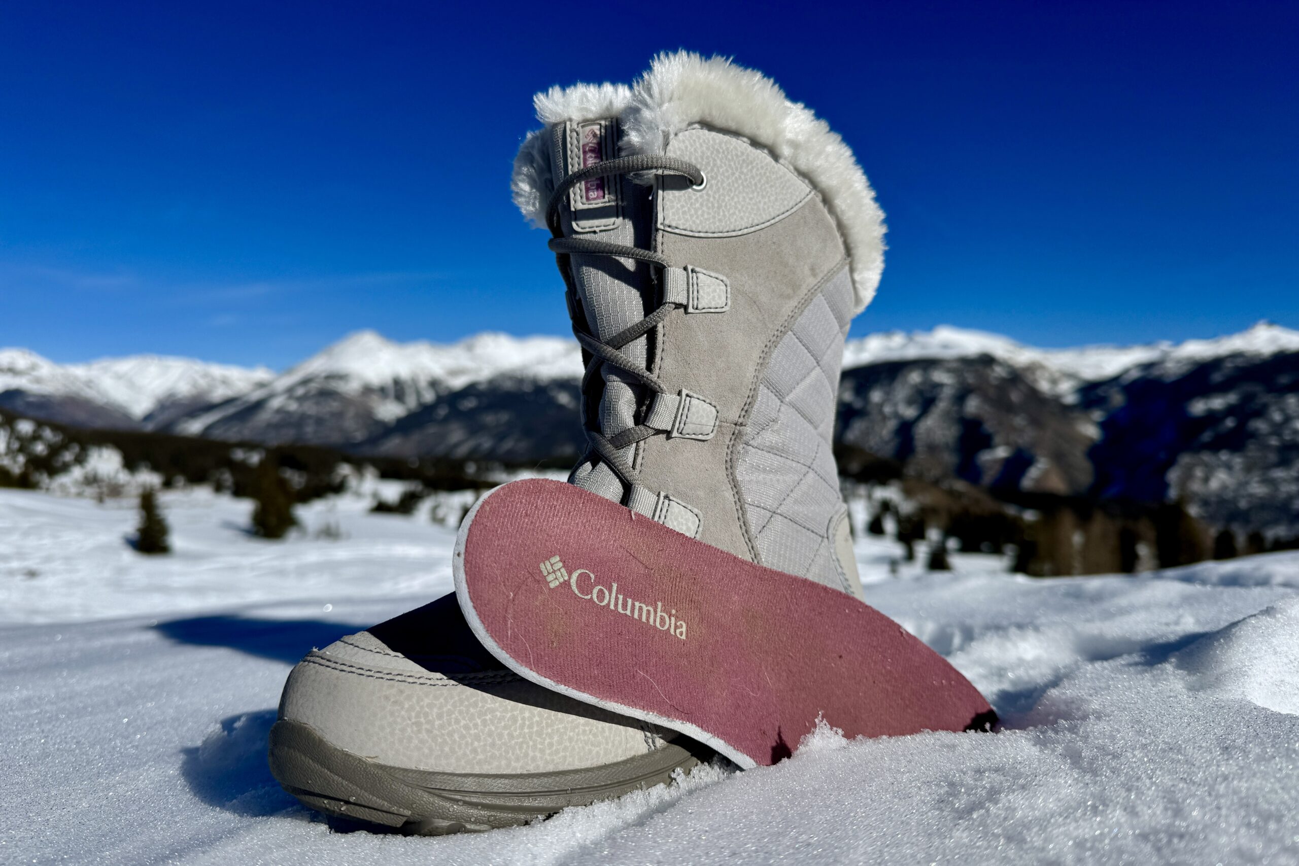 A close up of the Ice Maiden boot with the insole sitting next to it. They are set on some snow in the mountains.