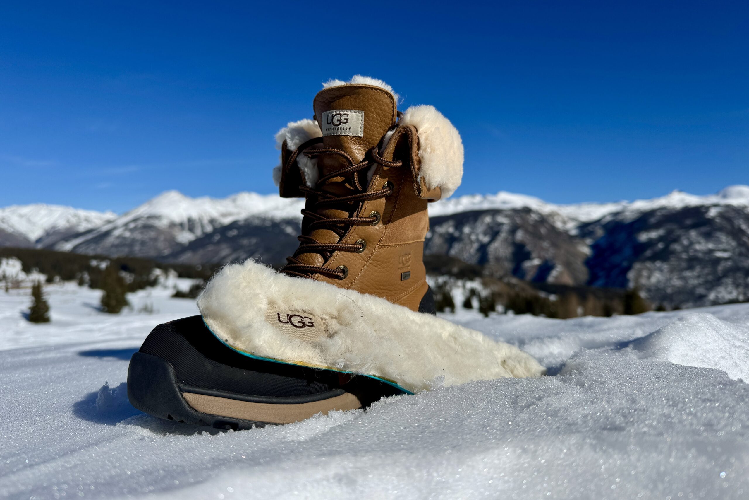 A close up of the UGG boot with the insole sitting next to it. They are set on some snow in the mountains.