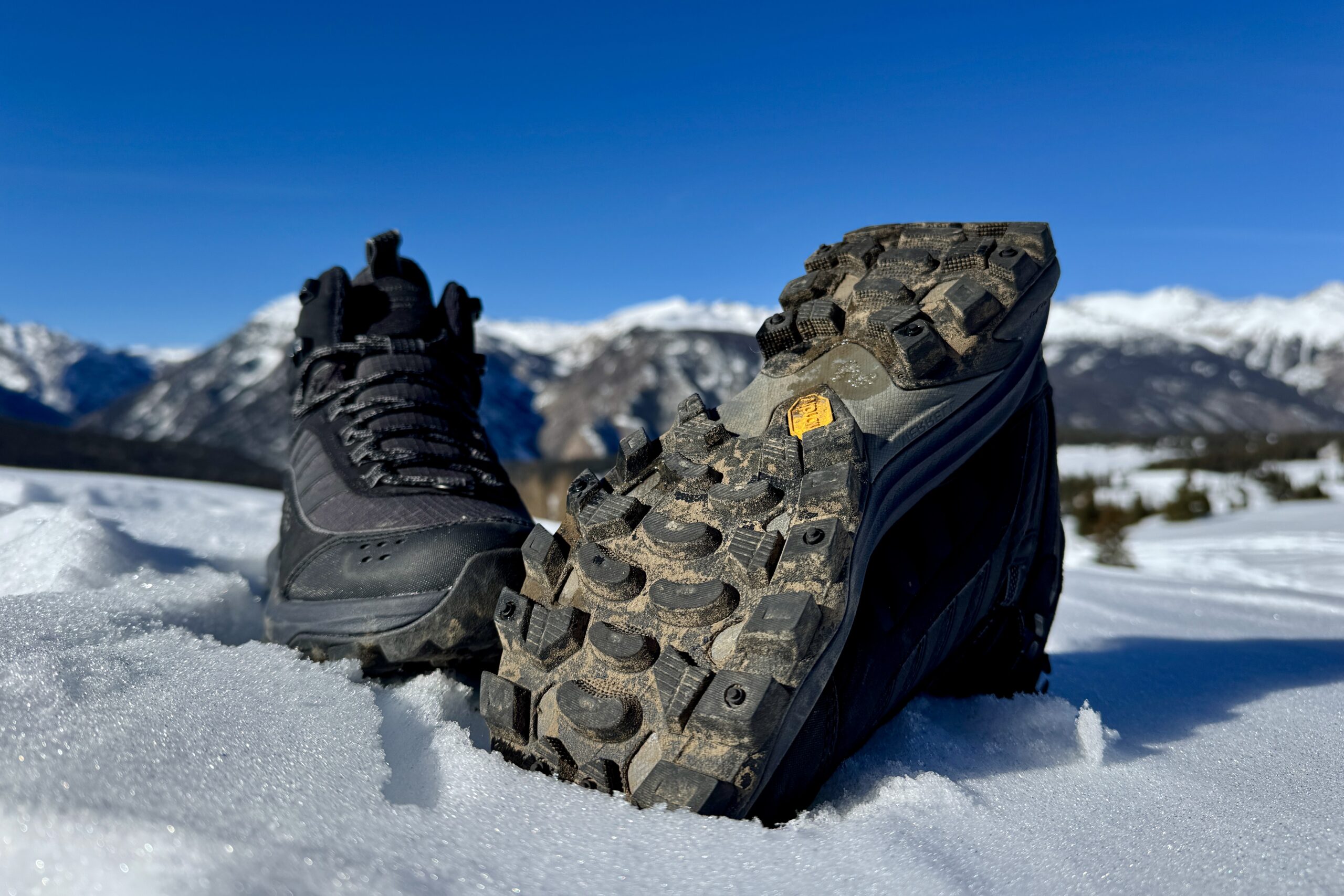 A close up of the tread on the bottom of the Merrell boot. It is sitting in the snow in the mountains.