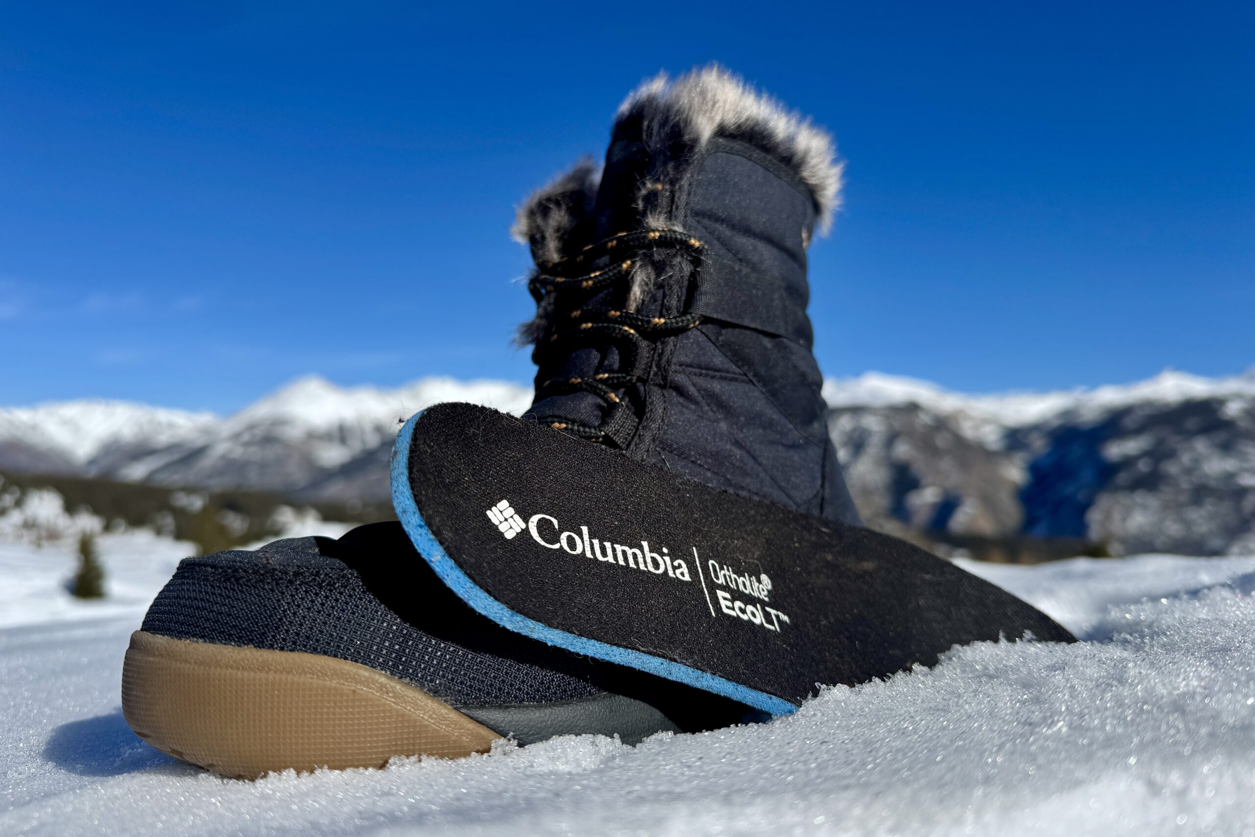 A close up of the Minx Shorty boot with the insole sitting next to it. They are set on some snow in the mountains.