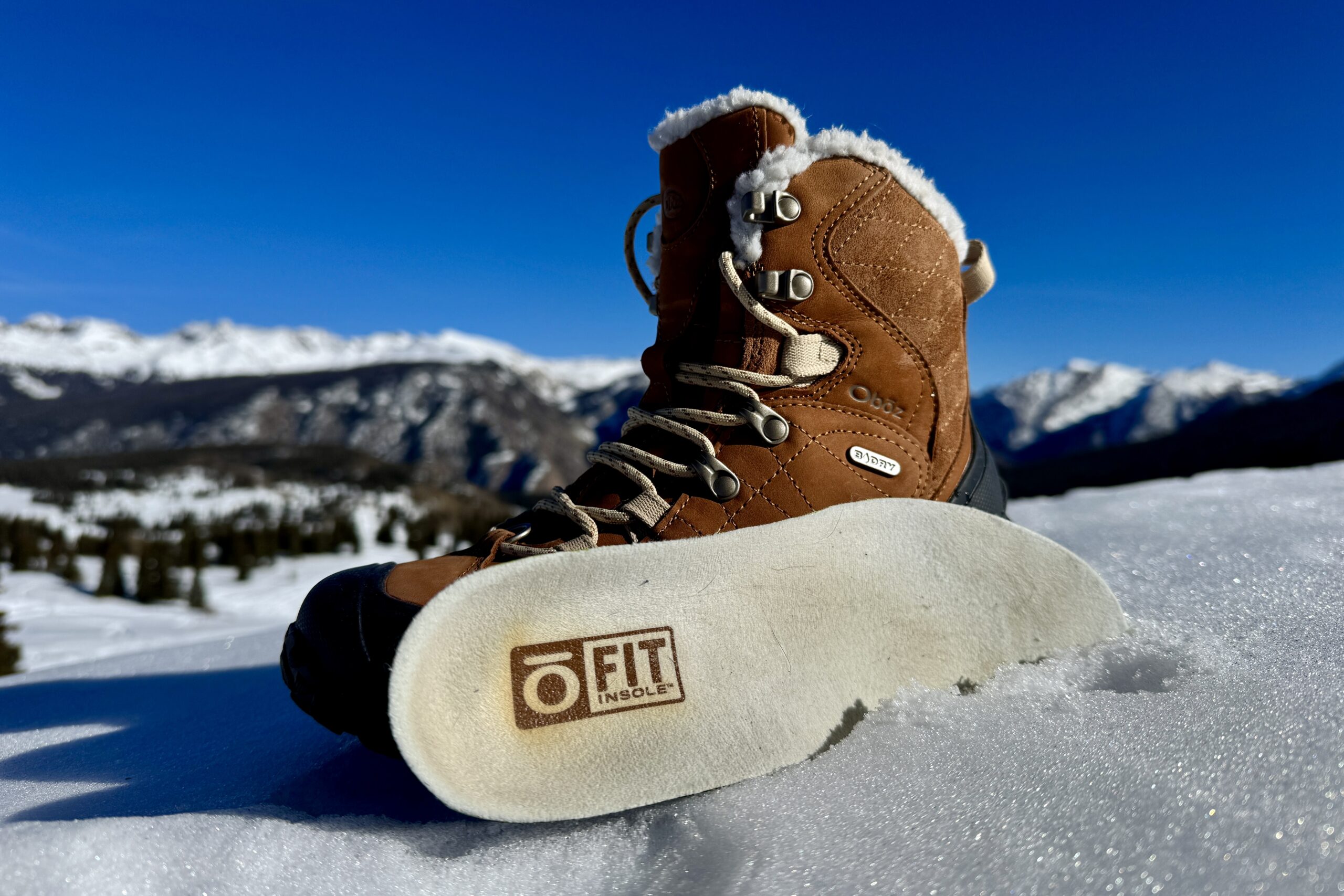 A close up of the Oboz boot with the insole sitting next to it. They are set on some snow in the mountains.