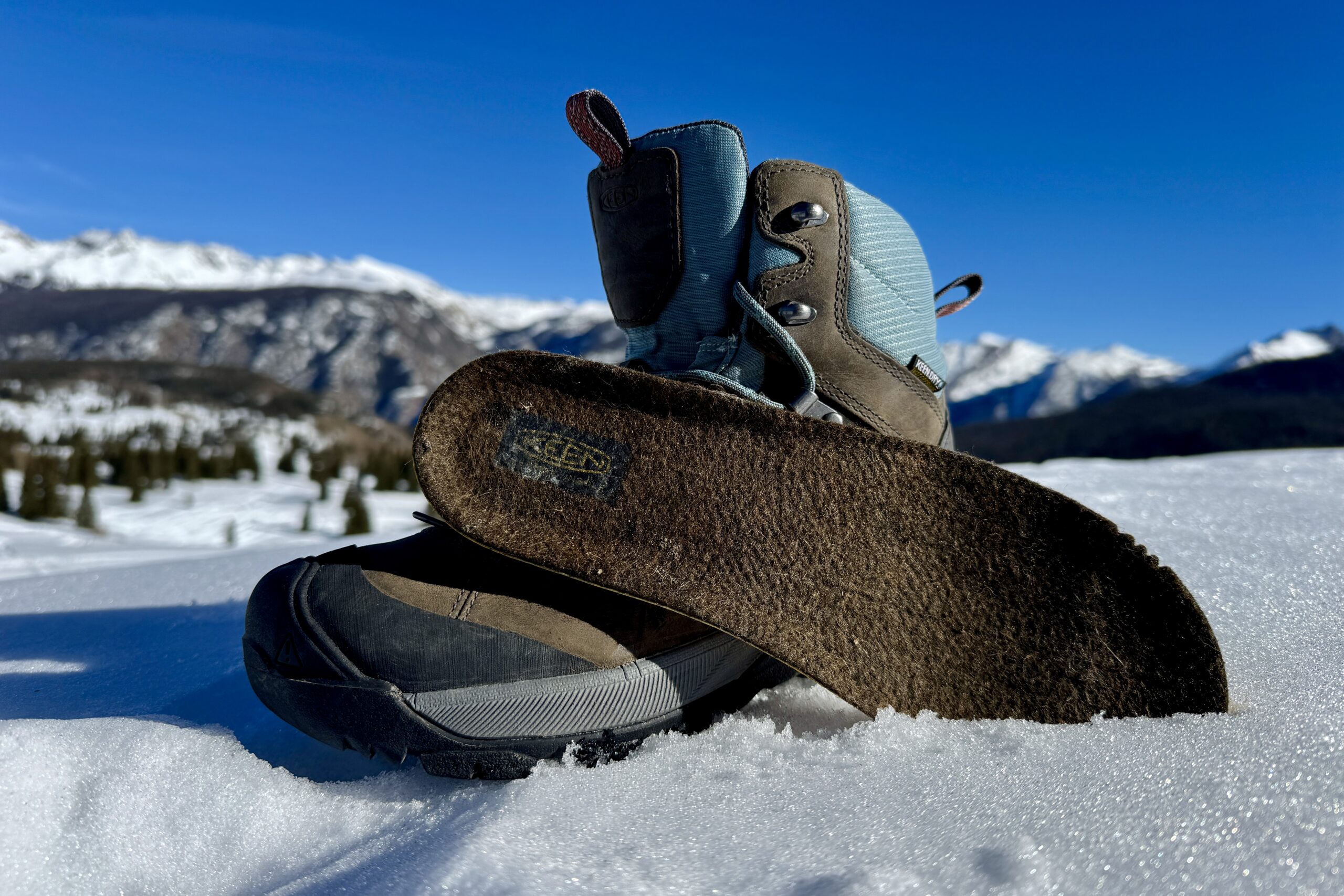 A close up of the Keen boot with the insole sitting next to it. They are set on some snow in the mountains.