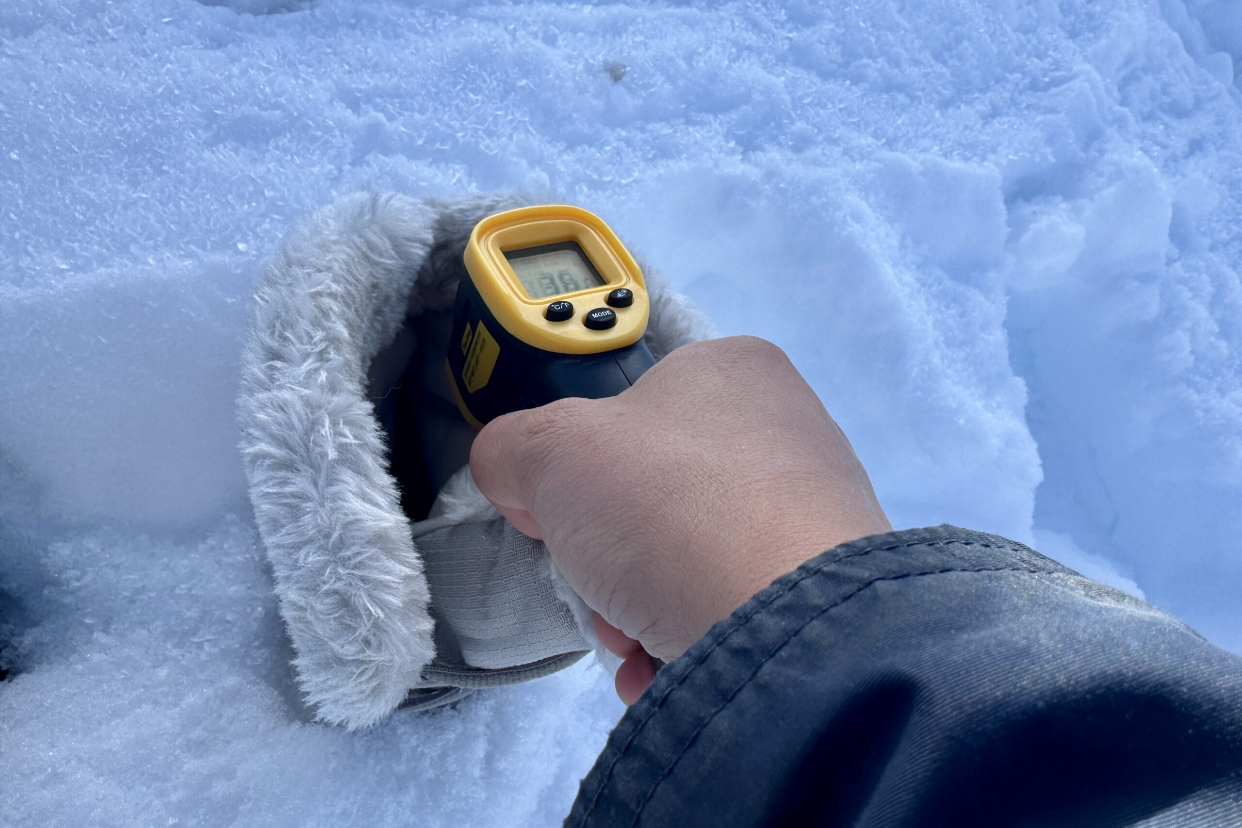 Close up of a hand pointing a laser thermometer into the Ice Maiden boot which is sitting in the snow.