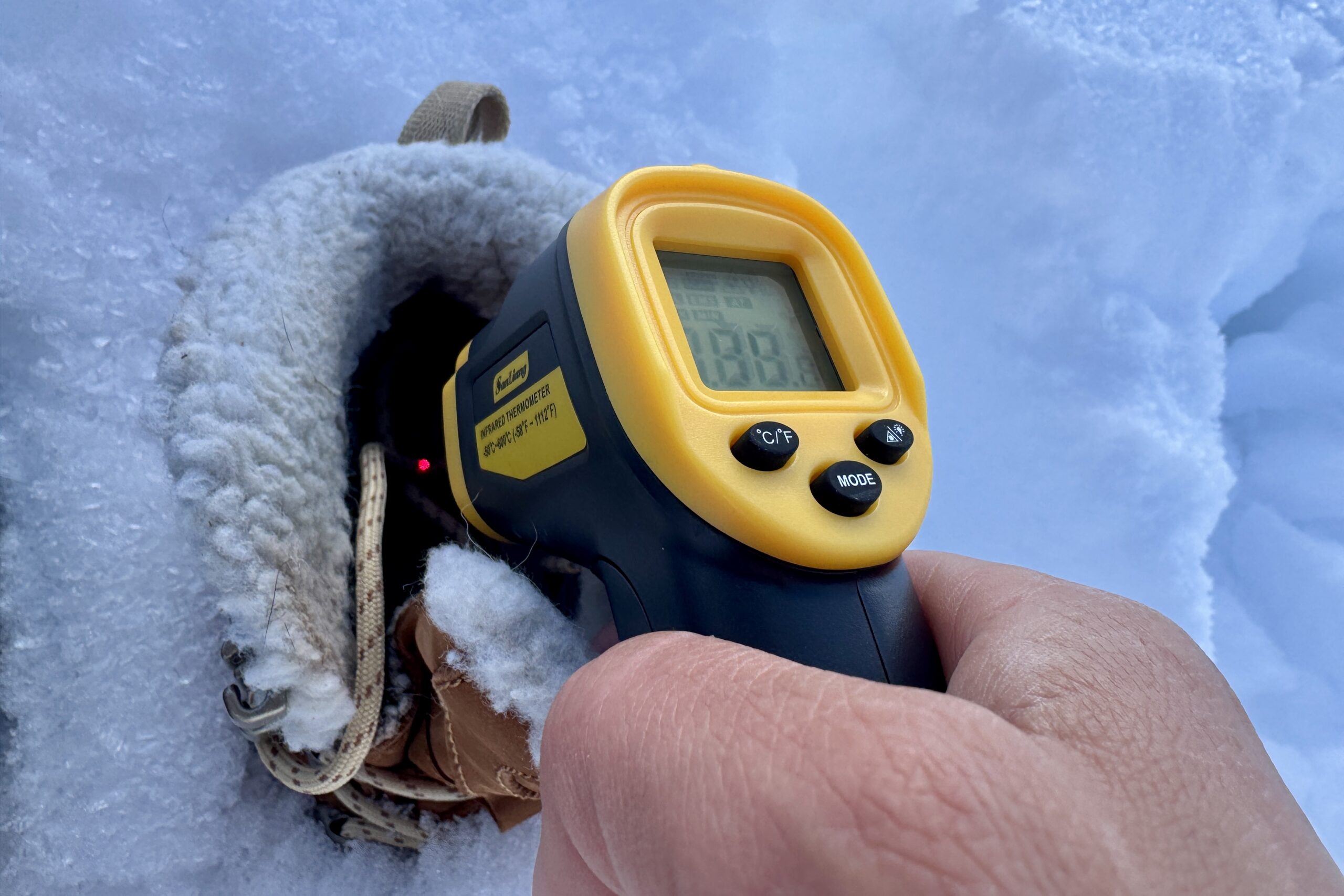 Close up of a hand pointing a laser thermometer into the Oboz boot which is sitting in the snow.