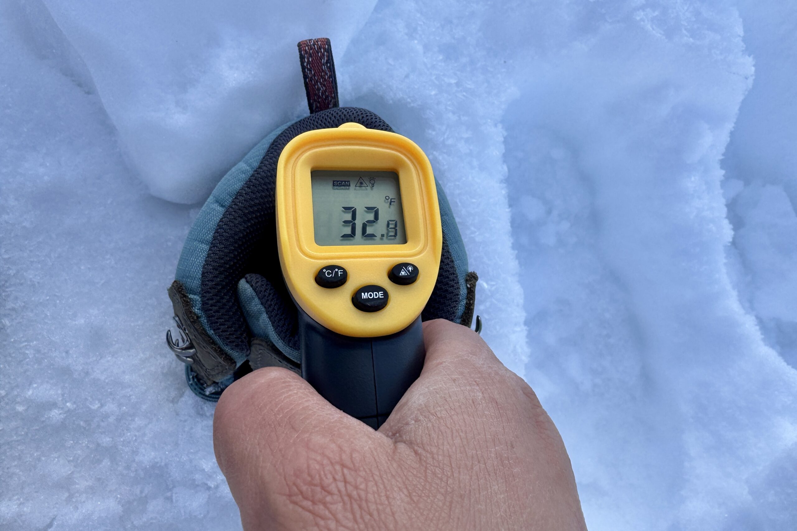 Close up of a hand pointing a laser thermometer into the Keen boot which is sitting in the snow.