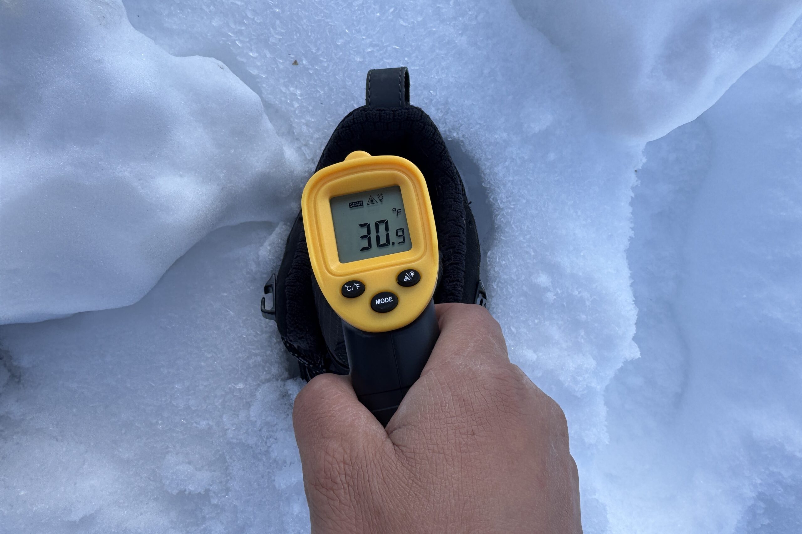 Close up of a hand pointing a laser thermometer into the Thermo Chill boot which is sitting in the snow.